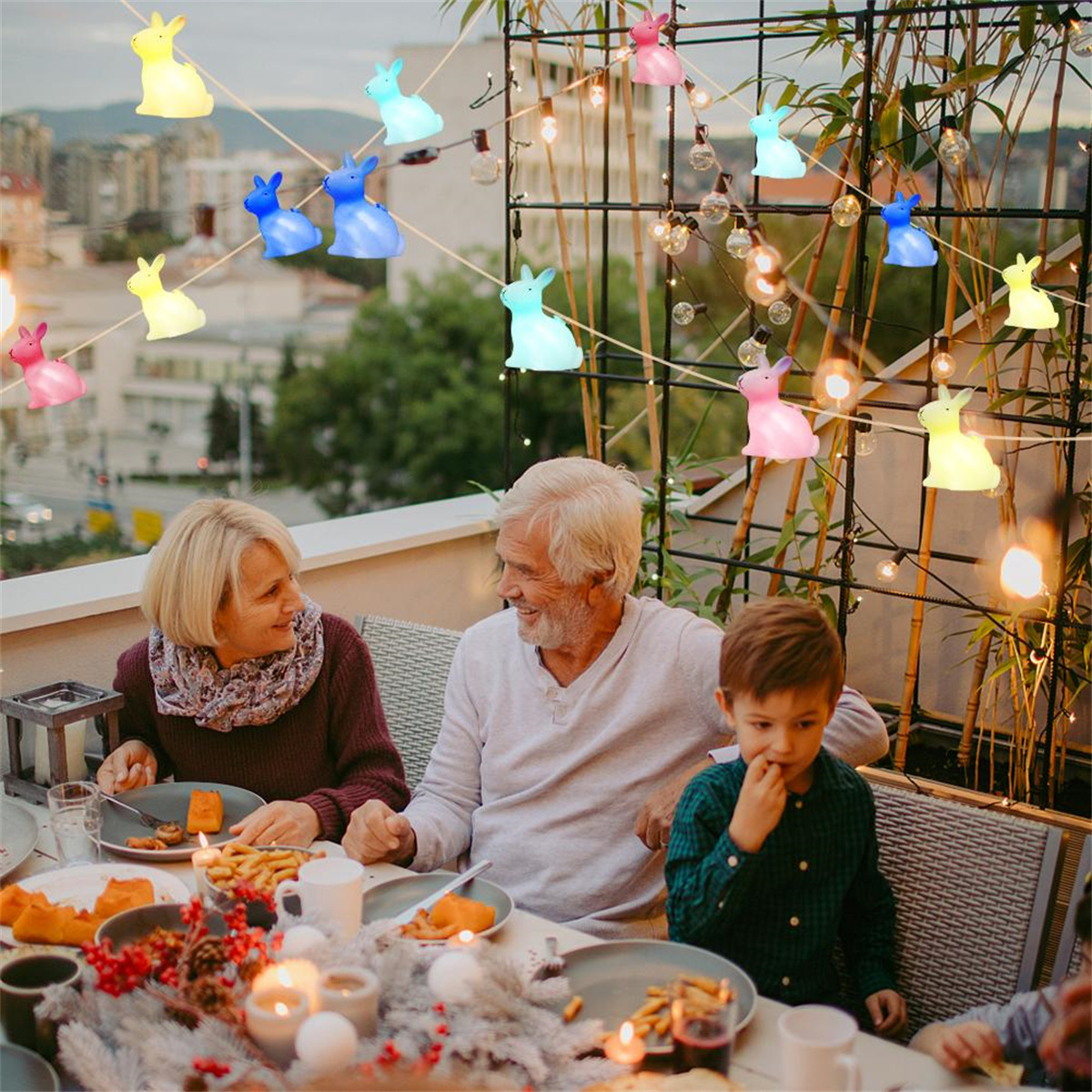 Eine Familie auf einer Terrasse, beleuchtet von Lichterketten. Sie essen und lächeln. Hasenlichter hängen über ihnen.