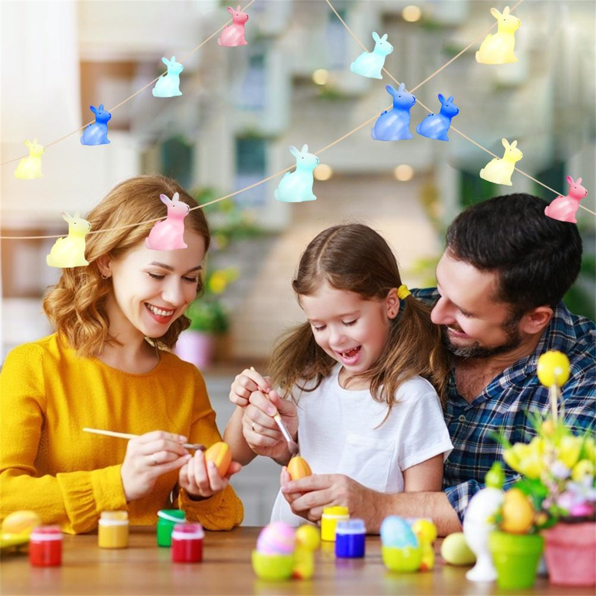 Eine Familie dekoriert Eier mit Farbe, während bunte Hasenlichter über ihnen hängen.
