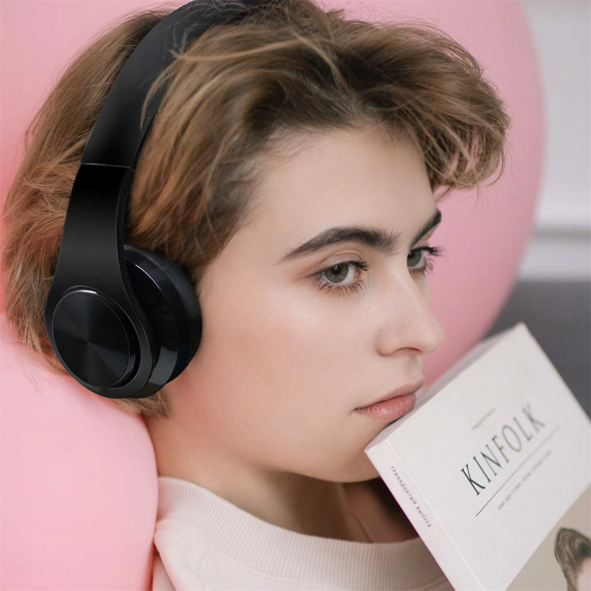 Frau mit schwarzen Kopfhörern, hält ein Buch mit dem Titel 'KINFOLK'.