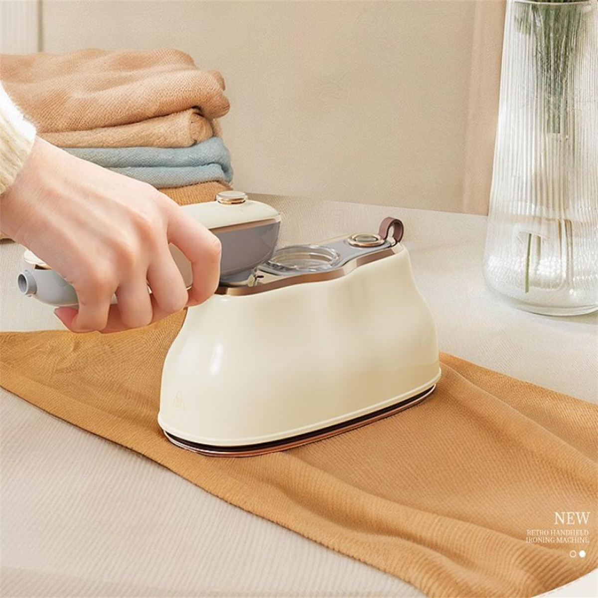 Eine Hand bügelt einen hellbraunen Stoff mit einem Retro-Handbügeleisen. Eine Vase ist im Hintergrund.