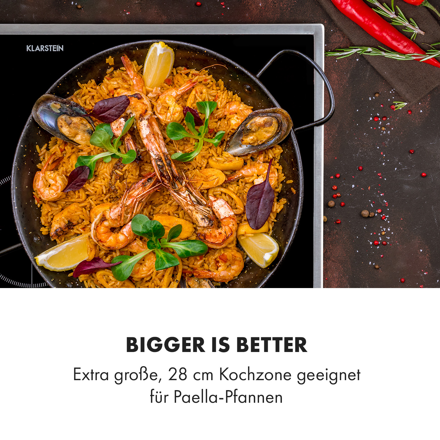 Paella mit Meeresfrüchten und Zitrone auf schwarzer Oberfläche, Kochplatte im Hintergrund.