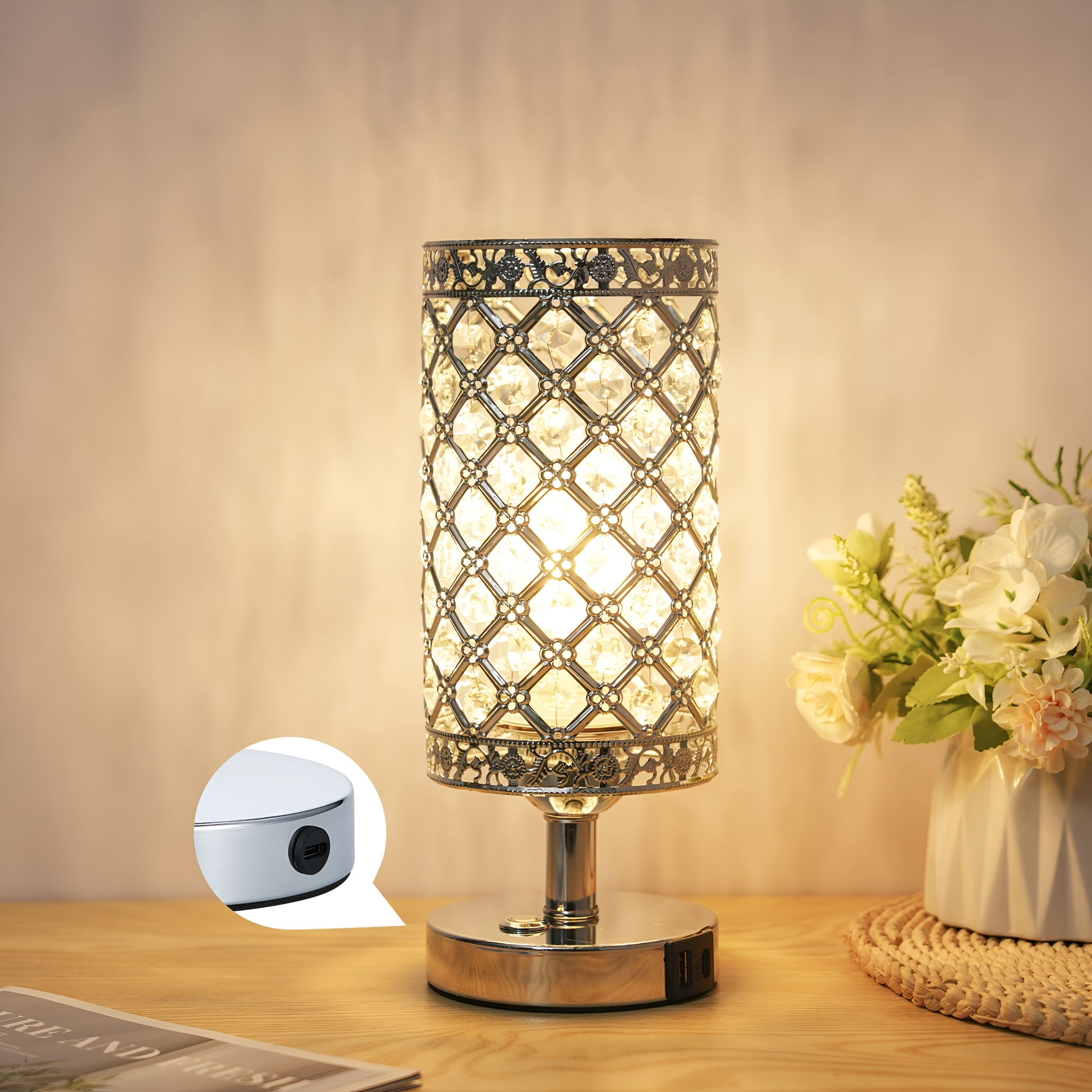 Eine dekorative Tischlampe mit zylindrischem, kristallbedecktem Schirm. Rechts eine Vase mit Blumen.