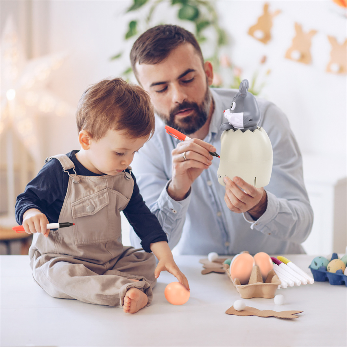 Vater und Sohn bemalen ein Ei mit einem Spielzeug-Häschen. Ostereier sind sichtbar.