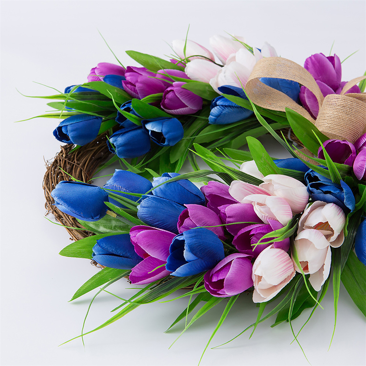 Ein Kranz aus künstlichen Tulpen in Blau, Lila und Weiß. Braune, gewebte Rankenbasis und grüne Blätter.