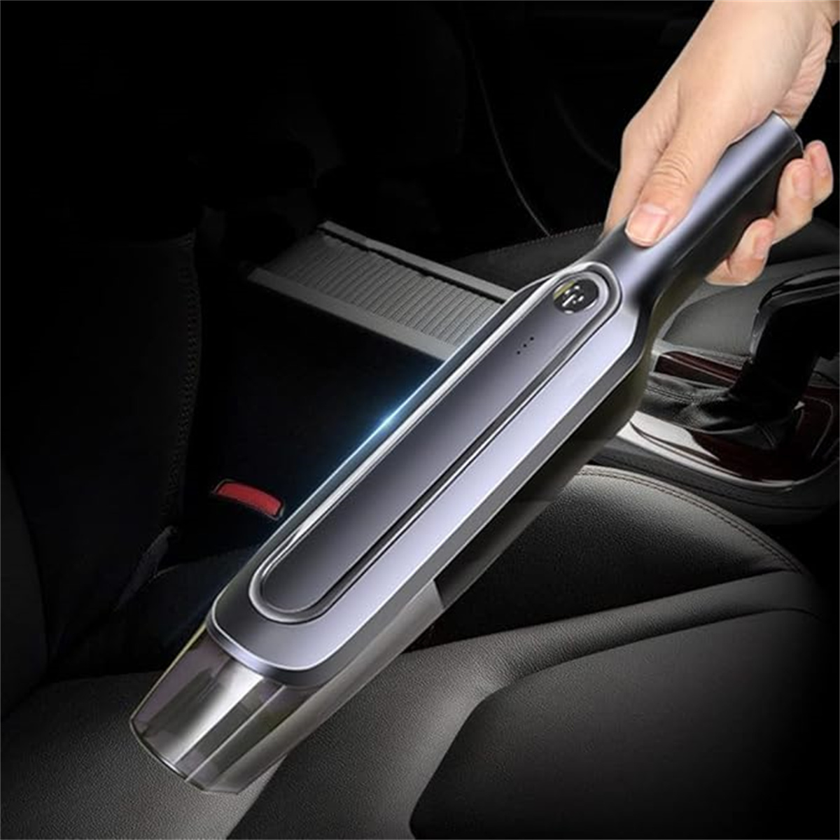 Hand hält einen Handstaubsauger. Sauberer, schwarzer Innenraum eines Autos im Hintergrund. Dunkle Umgebung.