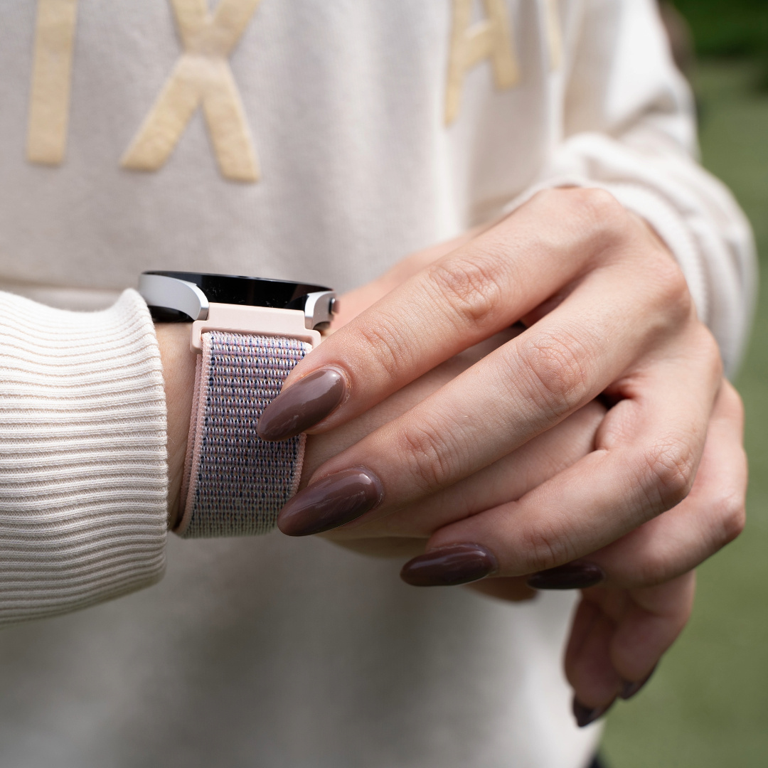 Nahaufnahme eines Handgelenks mit Smartwatch und hellrosa-blauem Armband.
