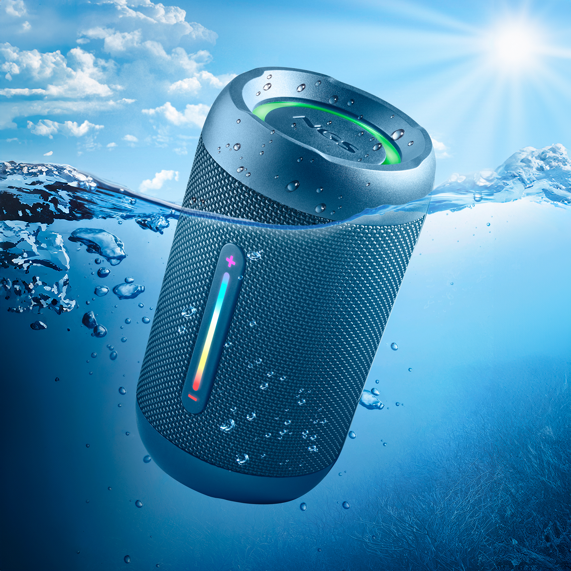 Niebieski głośnik wodoodporny zanurzony w wodzie z bąbelkami i słonecznym tłem.