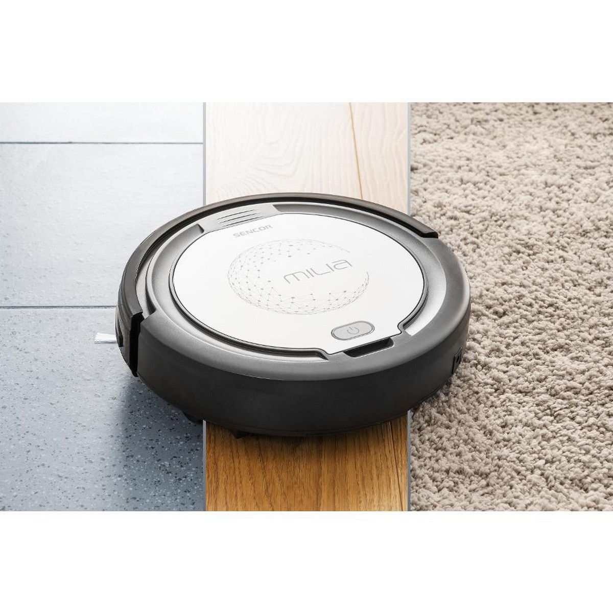 Aspirateur robot rond, noir et argent, sur sol en bois et moquette.