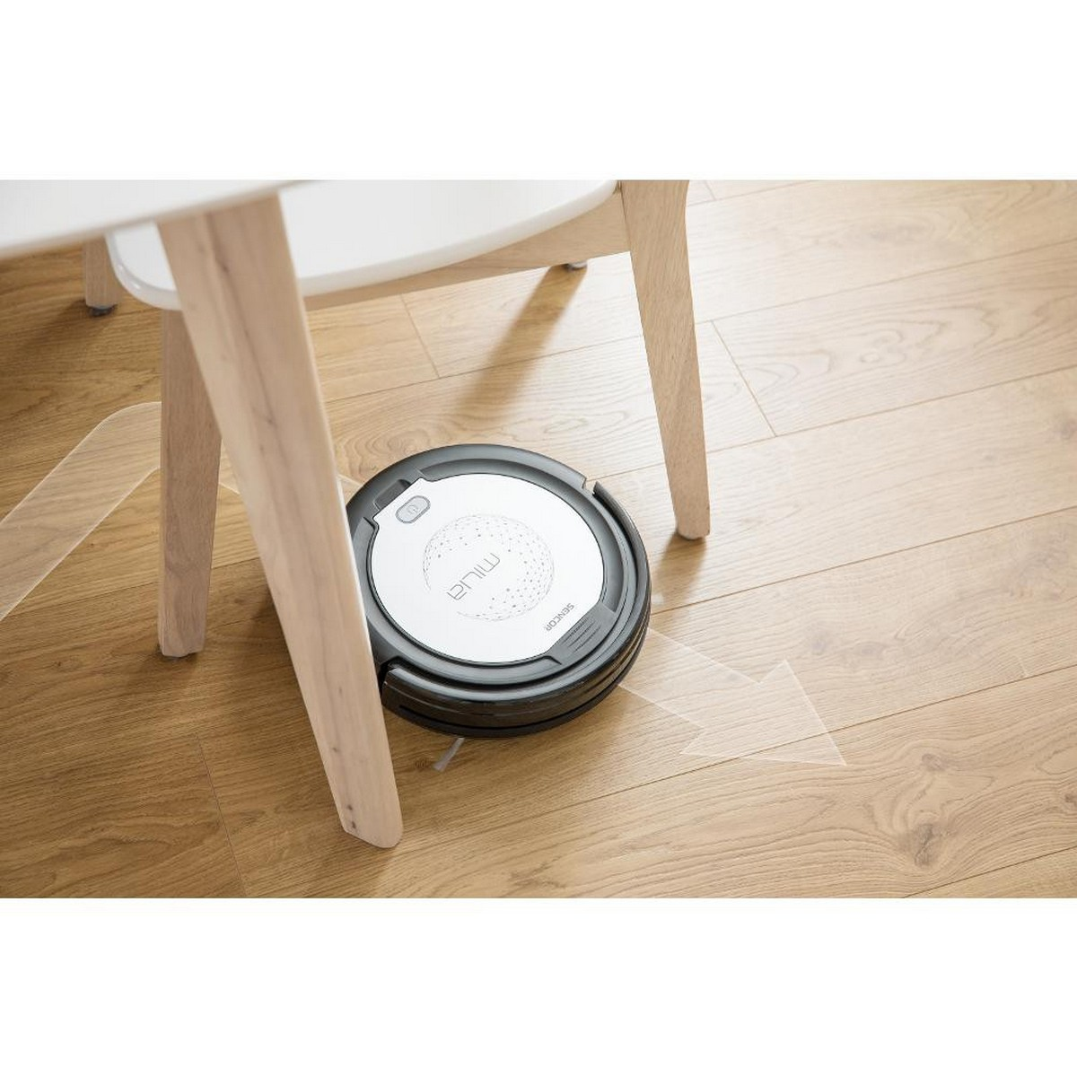 Robot aspirateur sous une table. Circulaire, noir et blanc, nettoyant un sol en bois.
