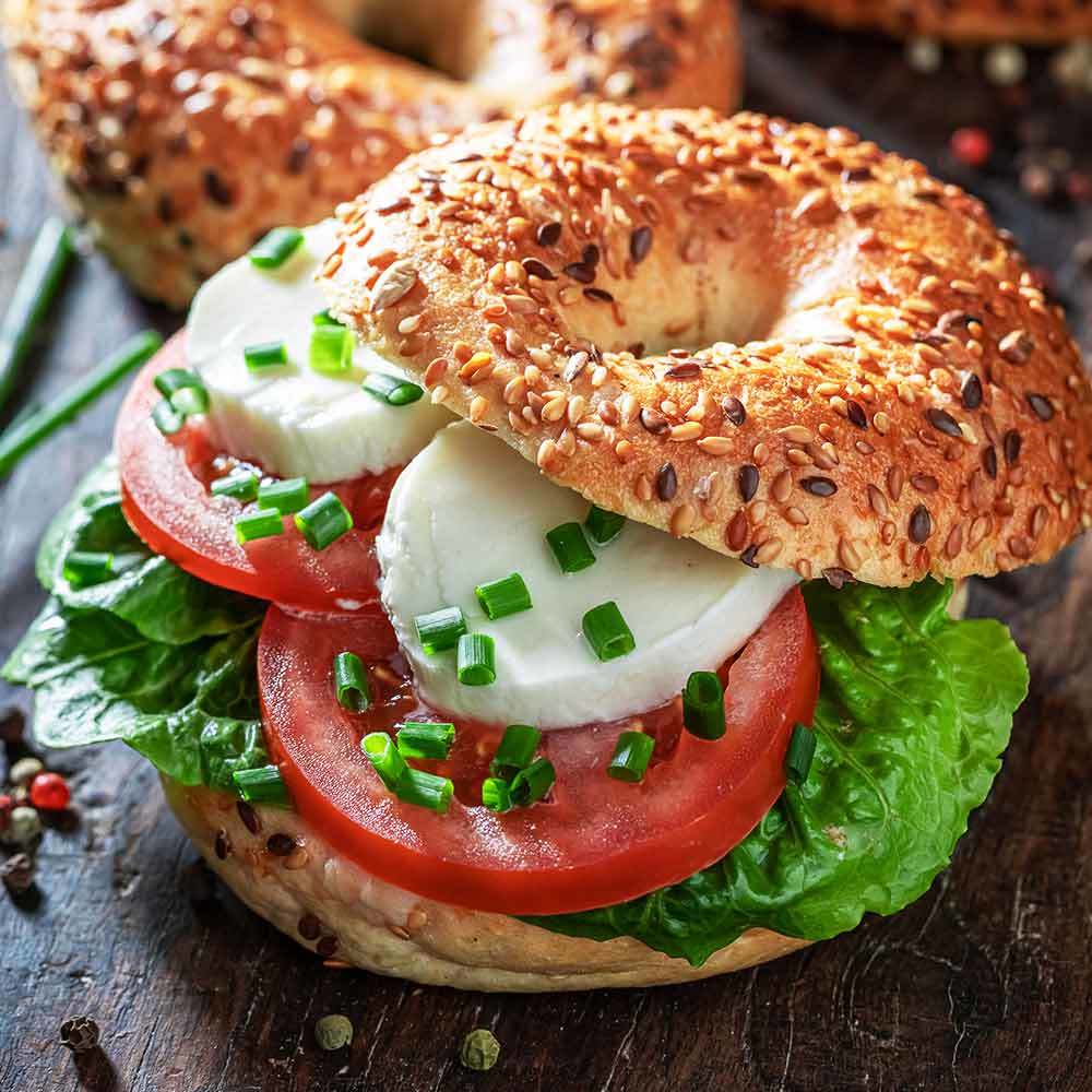 Bagel-Sandwich mit Mozzarella, Tomate, Salat und Gewürzen auf Holz.