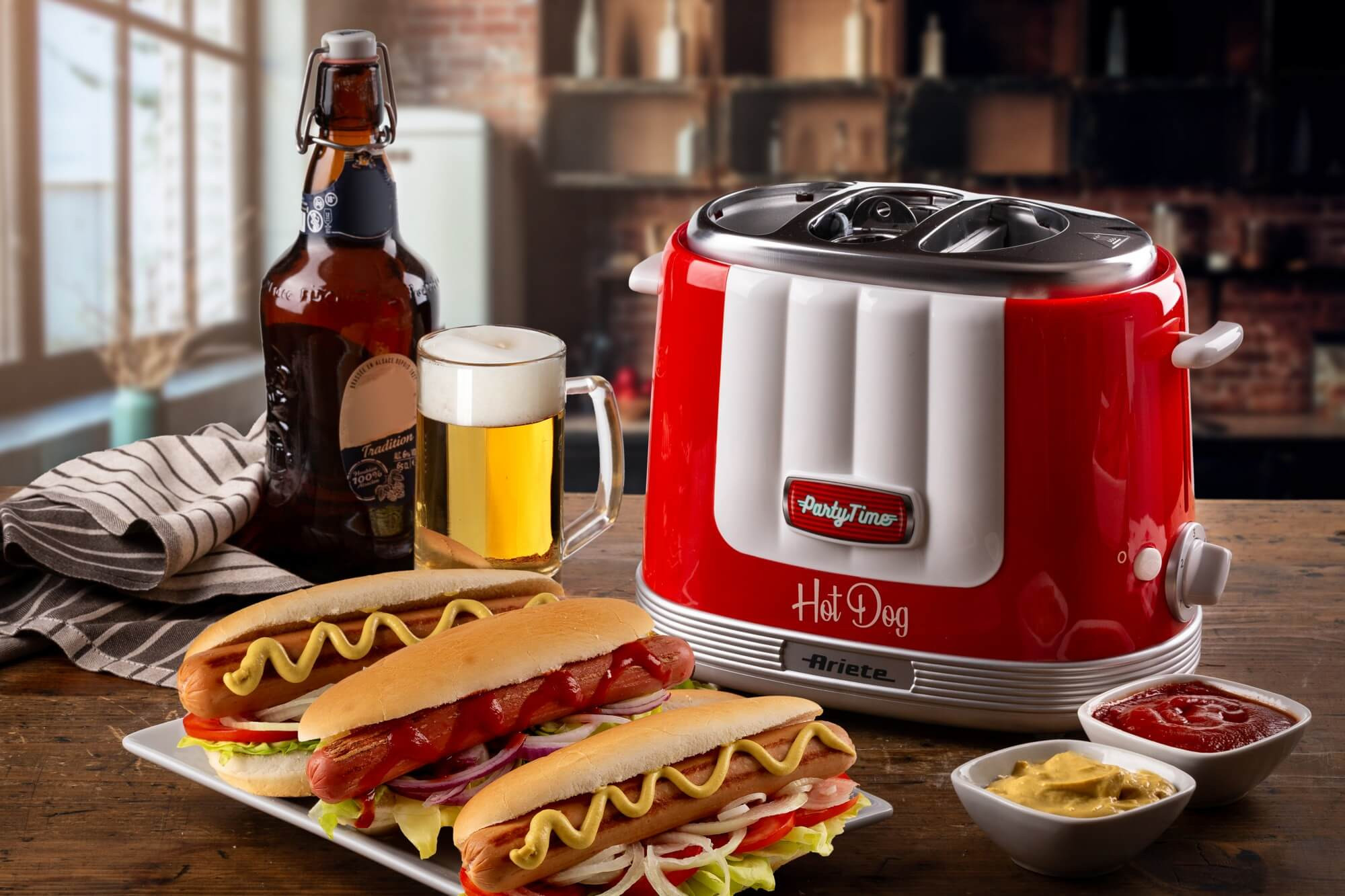 Hot dogs en un plato con condimentos, cerveza y una máquina de hot dogs roja al fondo.