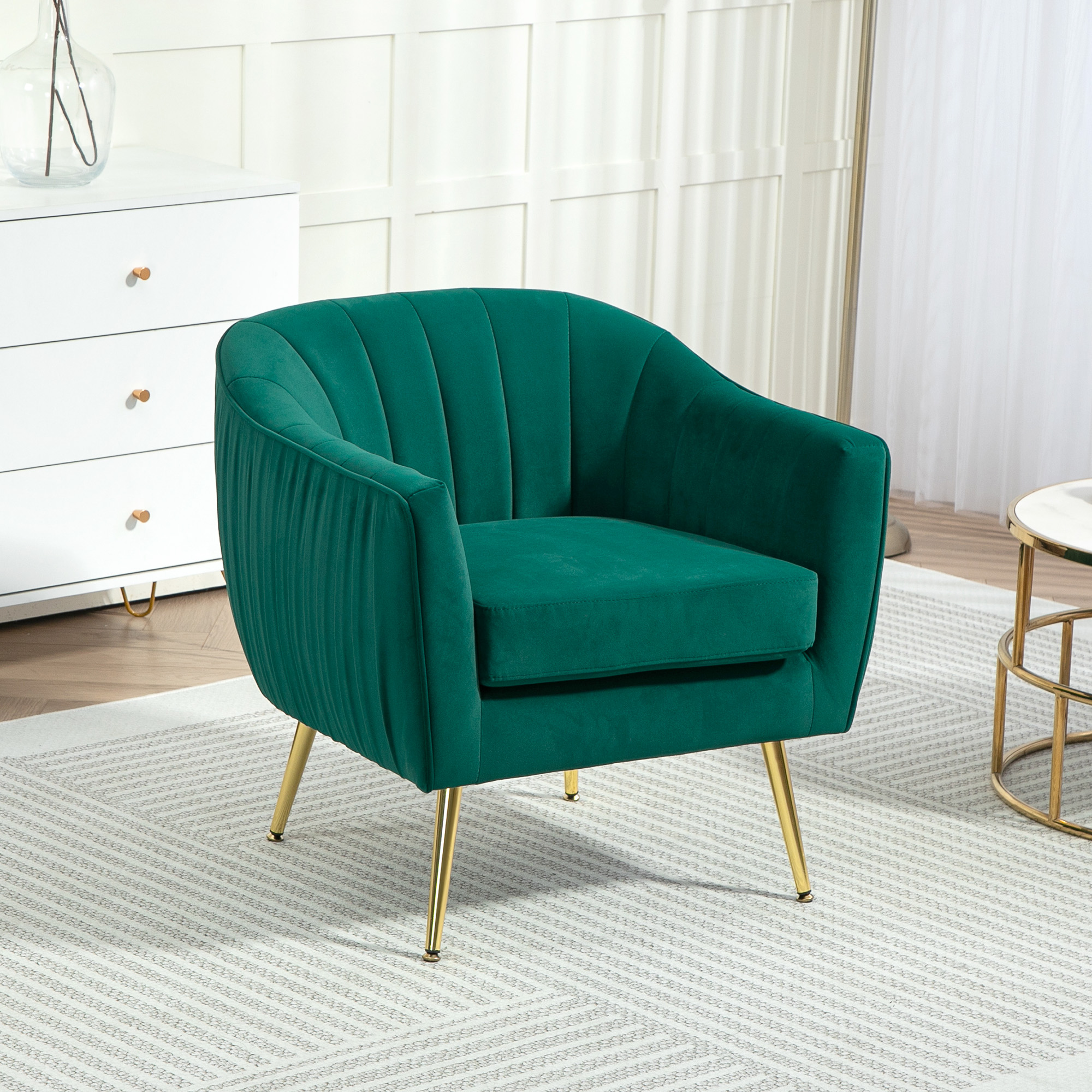Poltrona verde con gambe dorate, su un tappeto, mobile e tavolo bianchi sullo sfondo.