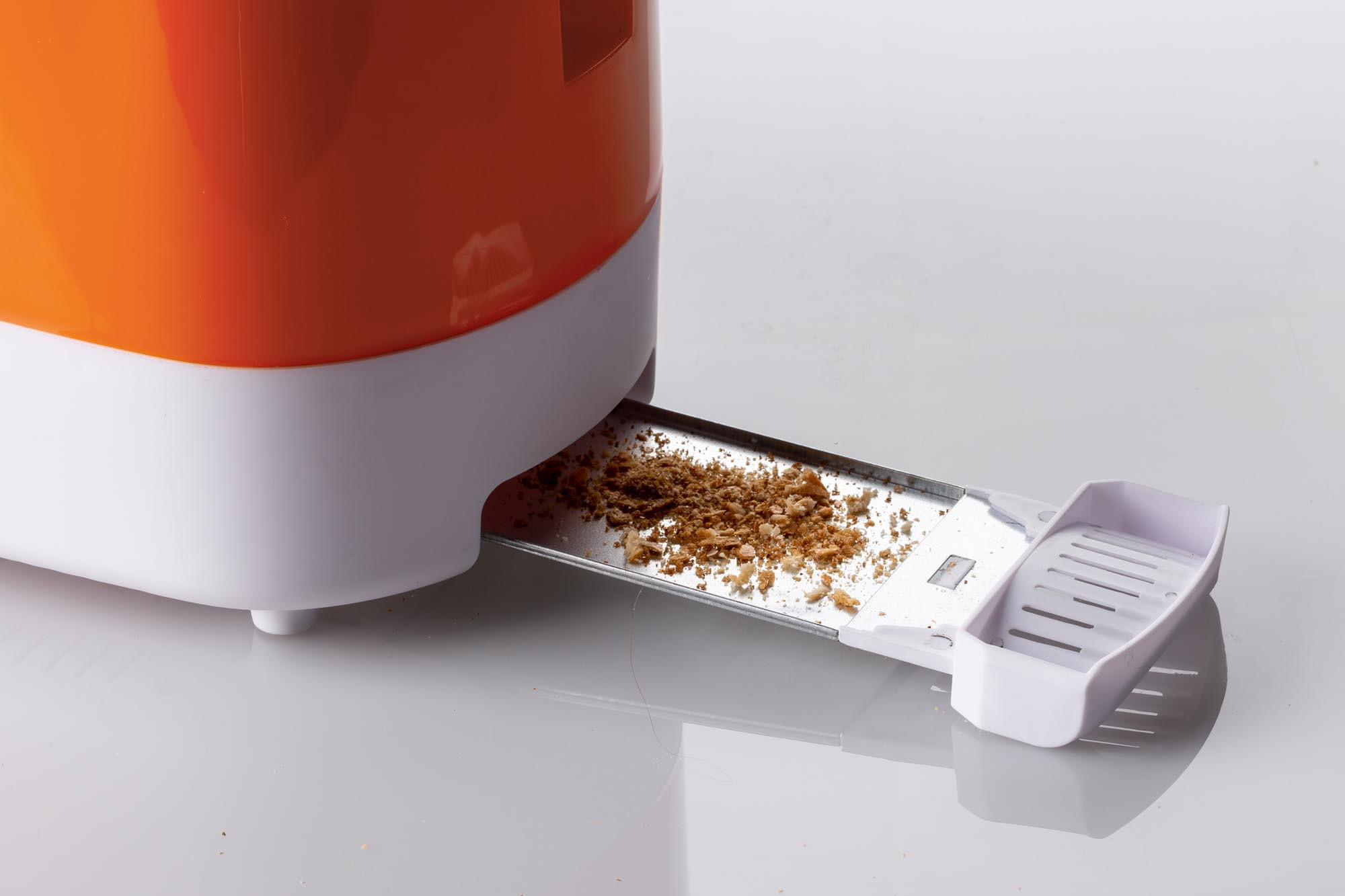Een close-up van een broodrooster met kruimels op de lade, wit en oranje design.