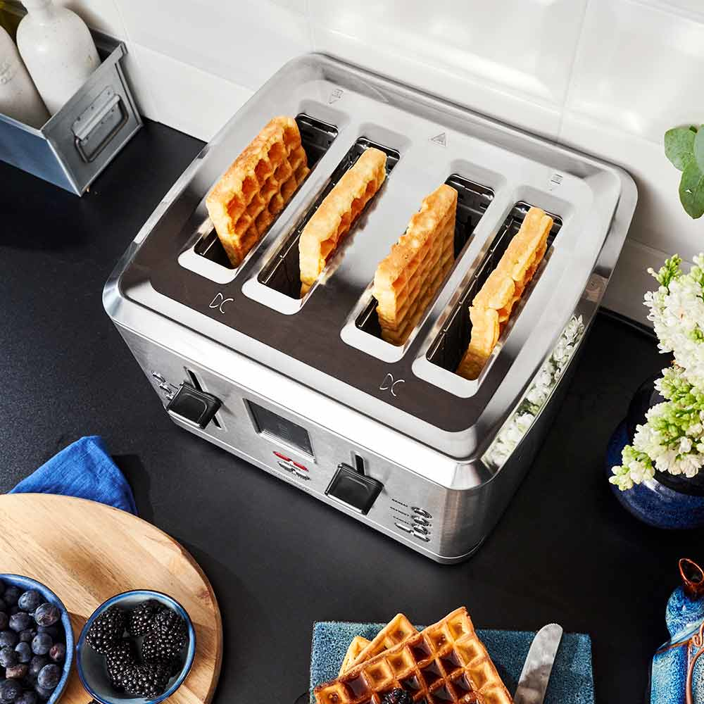 Un tostapane cromato con quattro waffle tostati all'interno, su un piano di lavoro nero.