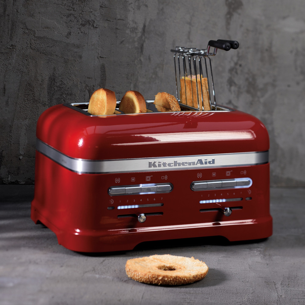 Kırmızı KitchenAid ekmek kızartma makinesi ve ekmek. Gri duvarın önünde tost makinesi.