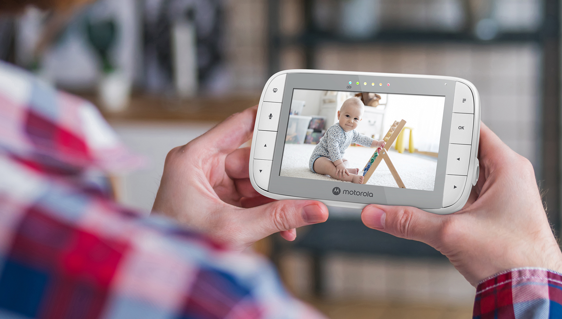 Eine Person hält einen Babyphone mit einem Baby auf einem Holzspielzeug.