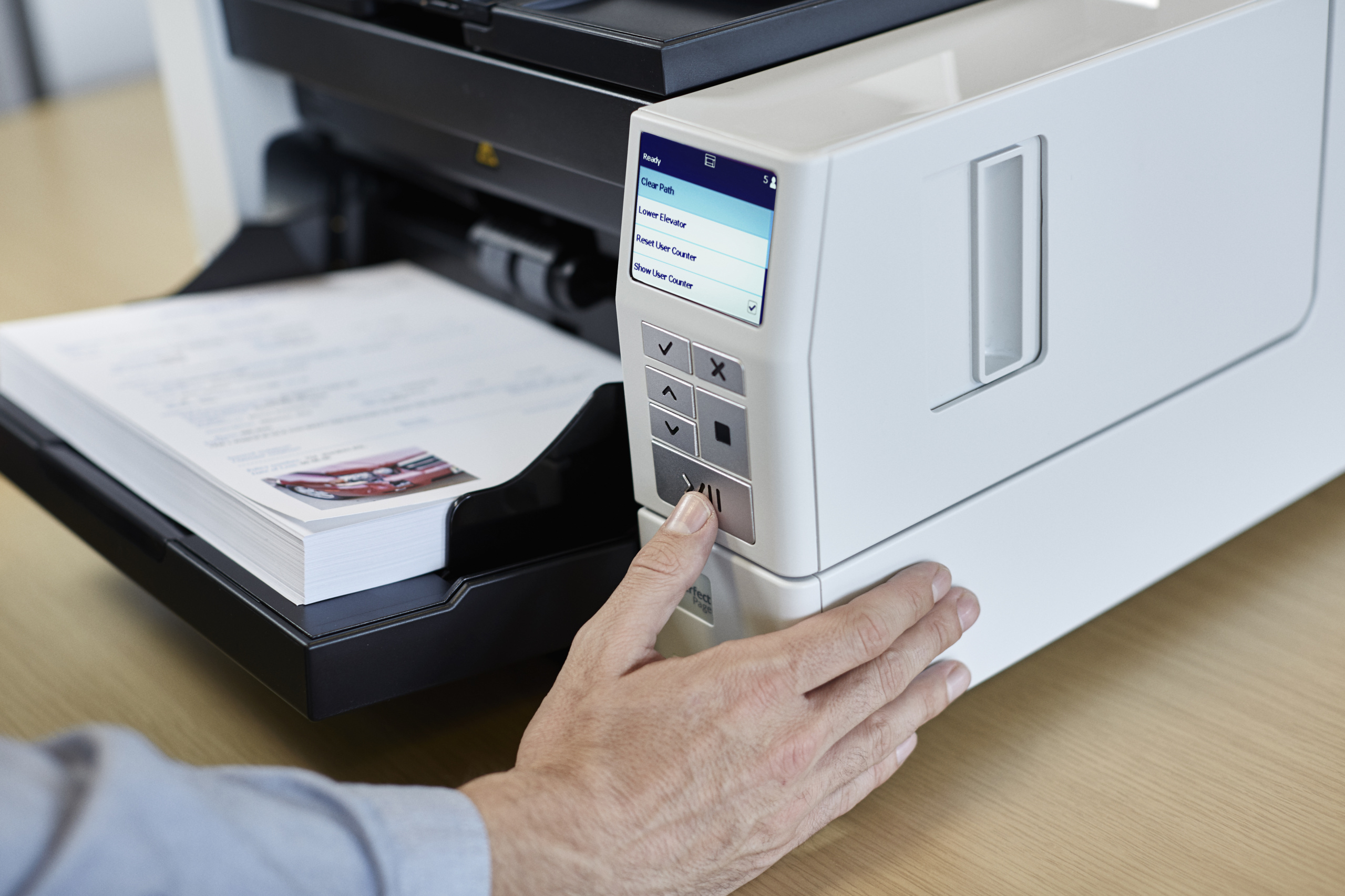 Mano che preme un pulsante su uno scanner bianco con documenti, su tavolo di legno.