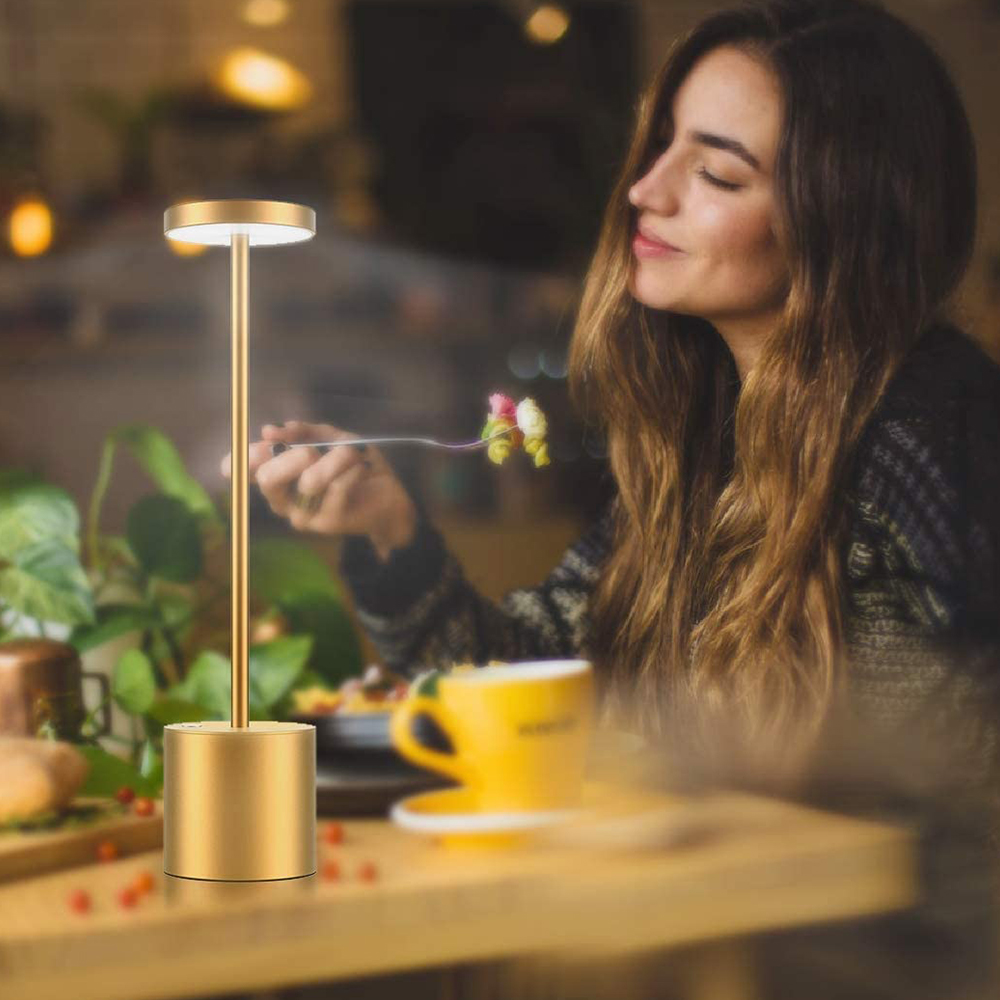 Eine Frau an einem Tisch mit einer goldenen Lampe und einer gelben Tasse, isst Essen.