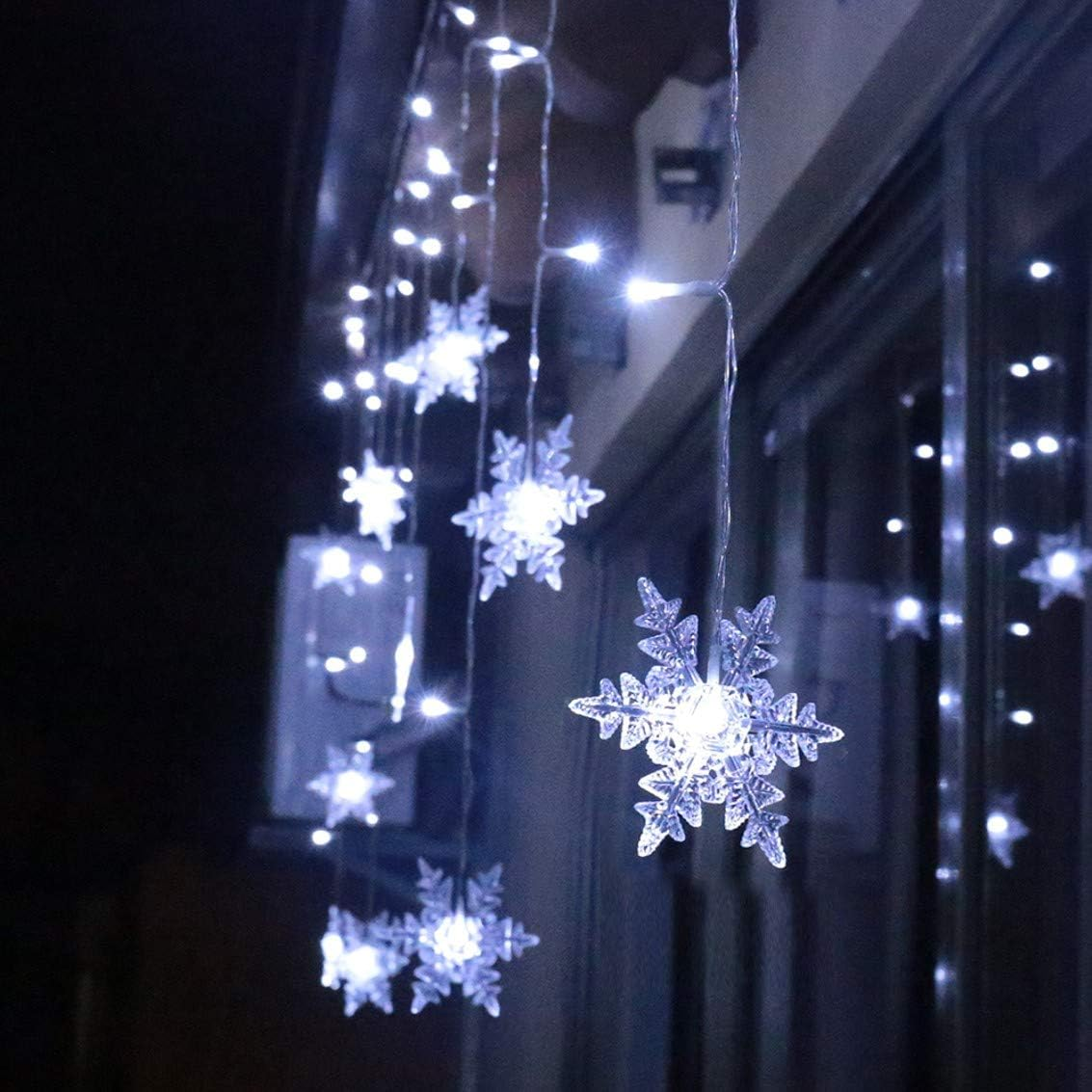 Lichterkette mit Schneeflocken hängt nachts draußen, leuchtet hell.