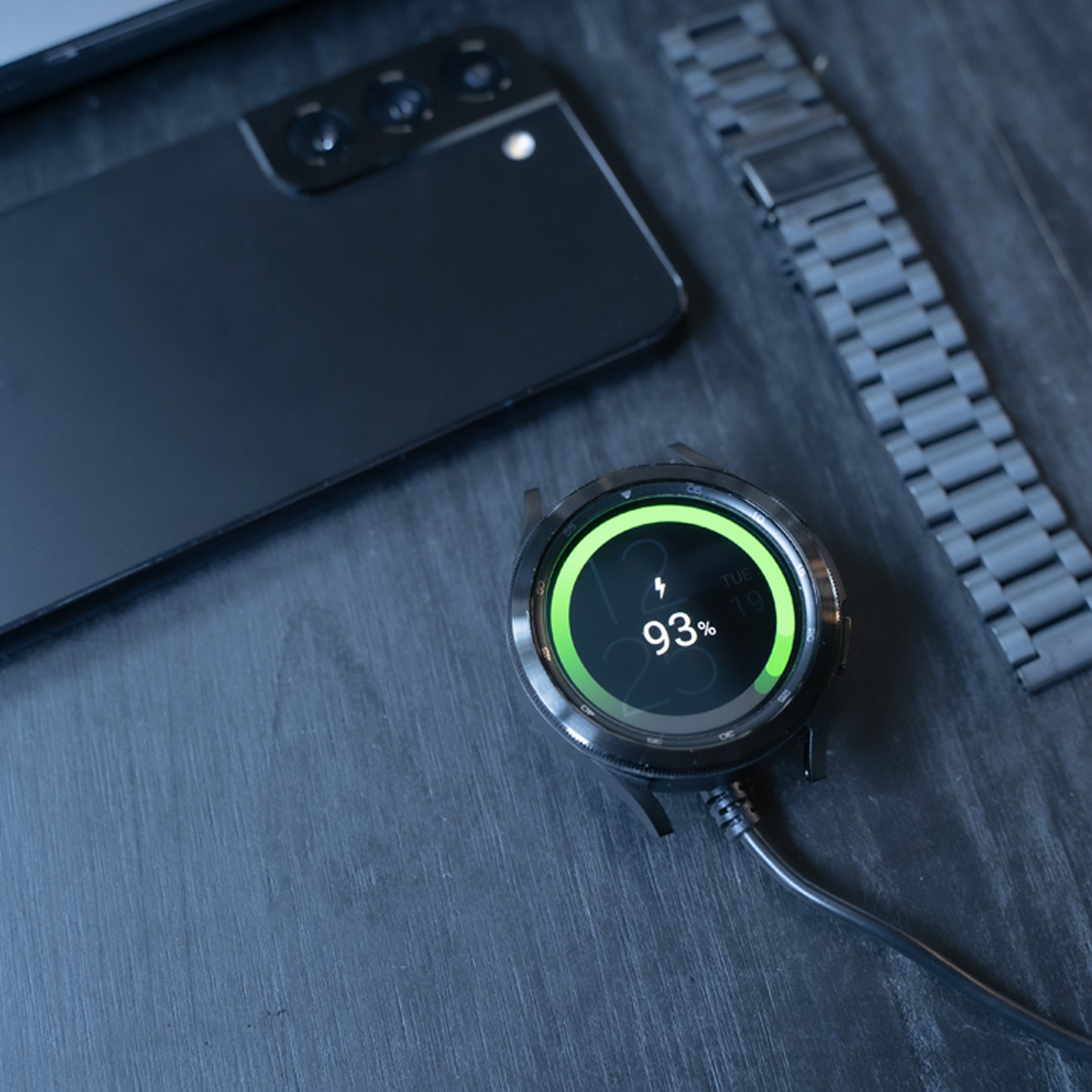 Schwarze Smartwatch, die mit einem grünen Kreis aufgeladen wird, und ein Telefon daneben. Schwarzer Hintergrund.