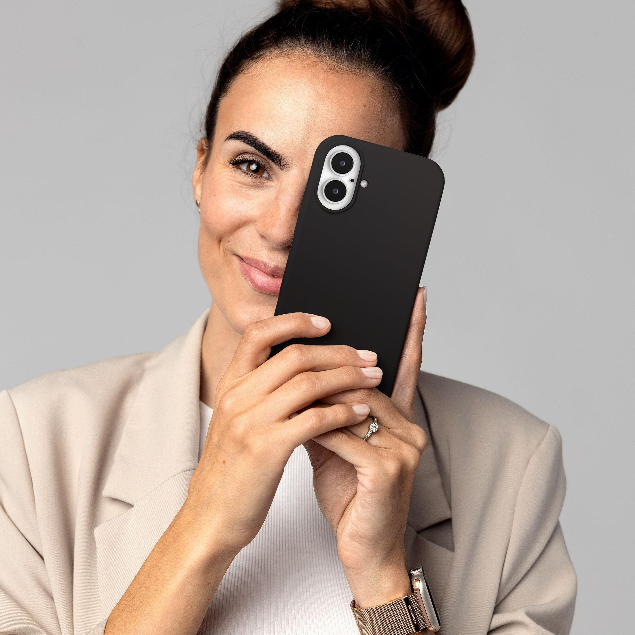 Femme tenant un téléphone noir, souriante. Elle porte une veste beige et a une montre et une bague.