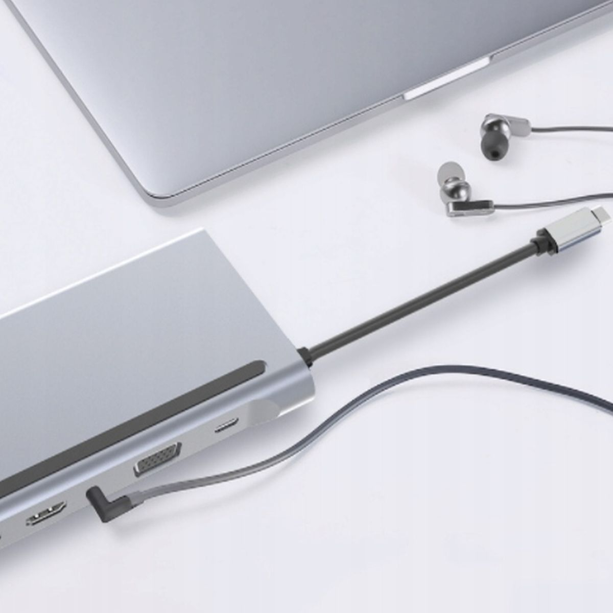 Srebrny hub z portami jest podłączony do laptopa i słuchawek na białej powierzchni.