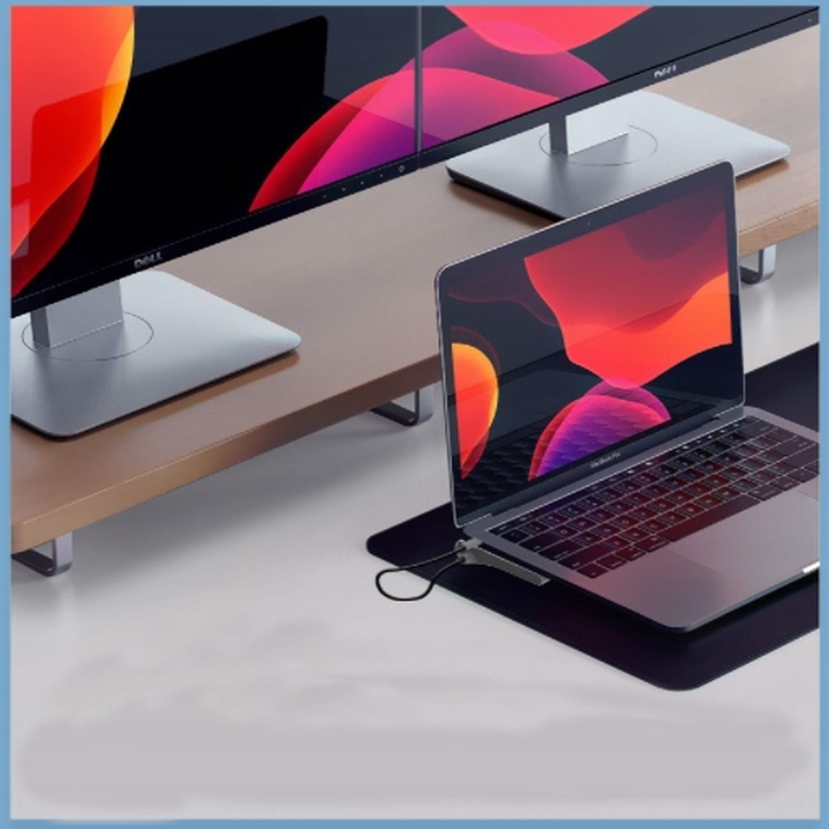 Laptop na czarnej podkładce, dwa monitory na drewnianym stojaku. Niebieskie tło.