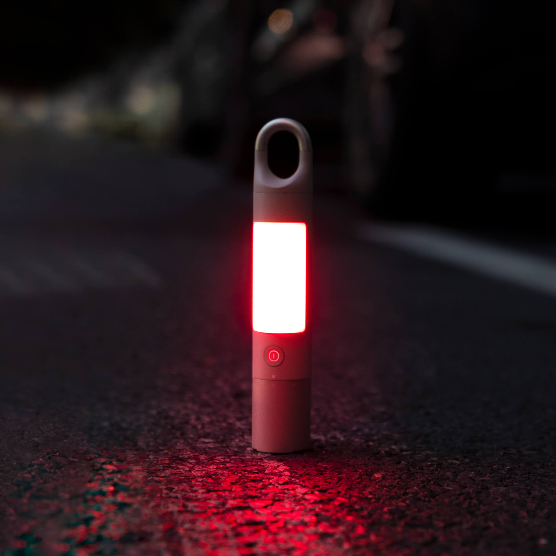 Eine rote Taschenlampe leuchtet auf einer dunklen Straße. Die Taschenlampe ist beleuchtet und zylindrisch.