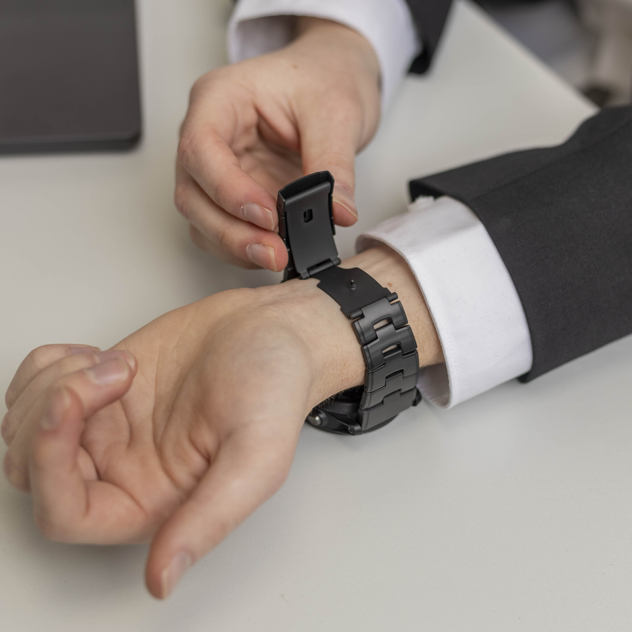 Die Hand einer Person, die eine schwarze Uhr an ihrem Handgelenk einstellt. Die Uhr hat ein Metallband.