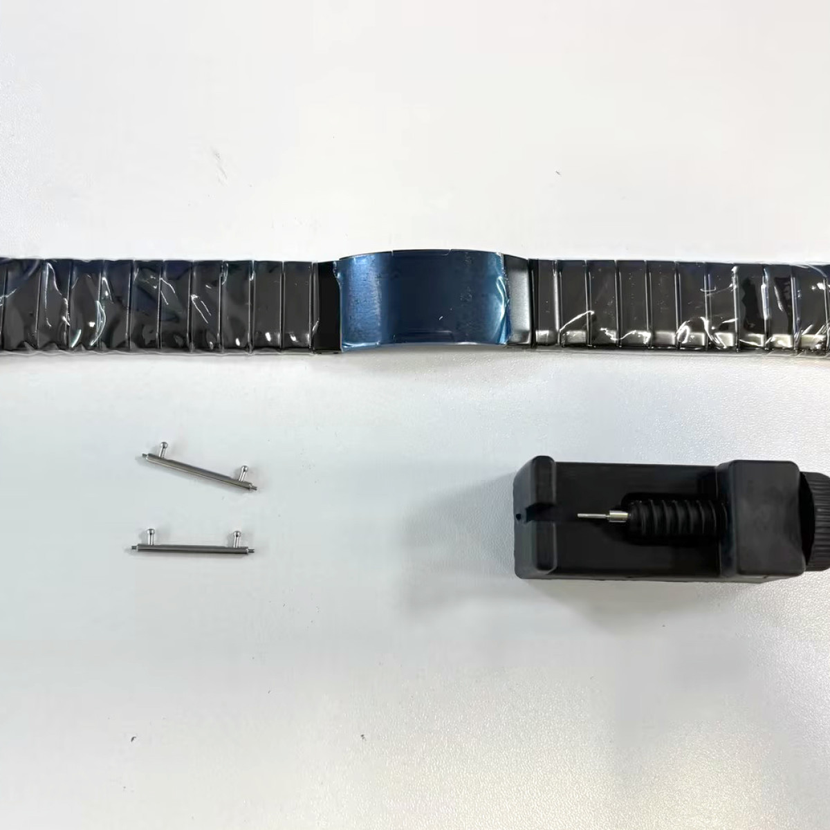 Horlogeband met pinnen en gereedschap op wit oppervlak.