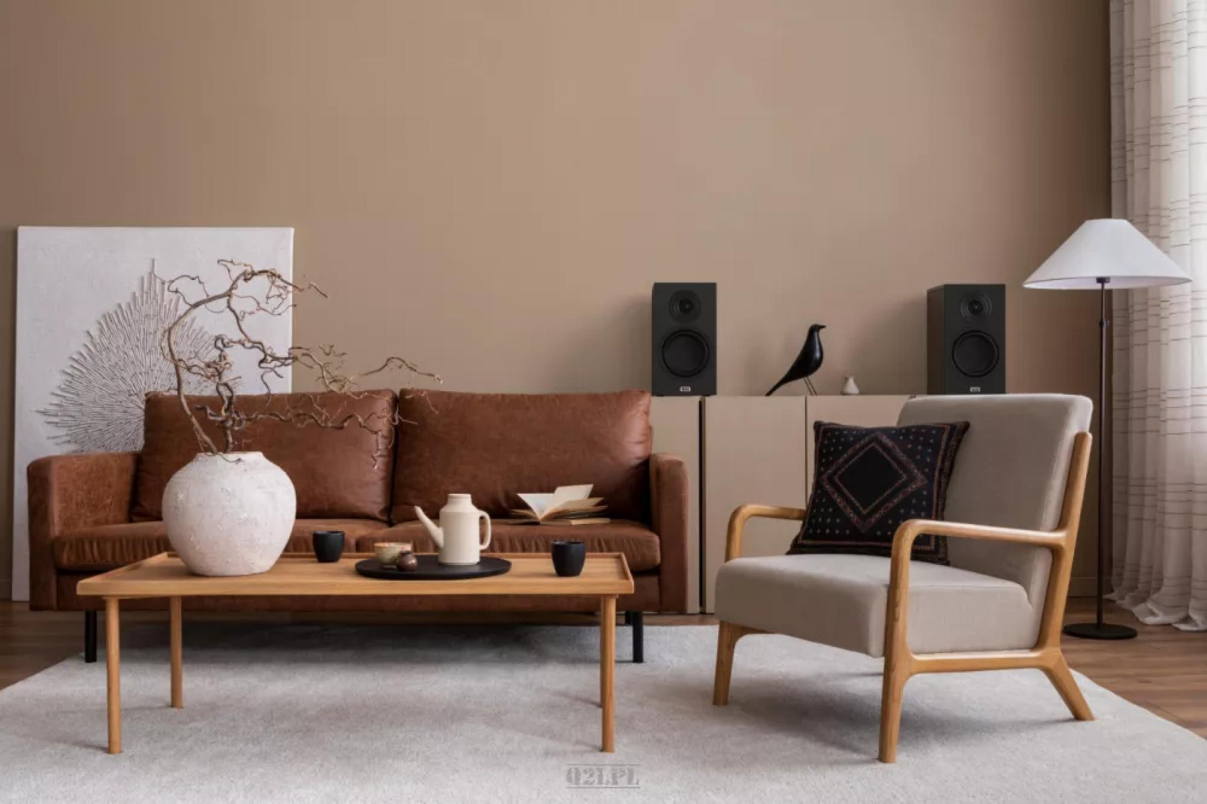 Wohnzimmer mit braunem Sofa, Holztisch, Lautsprechern und Stuhl. Die Wände sind beige.