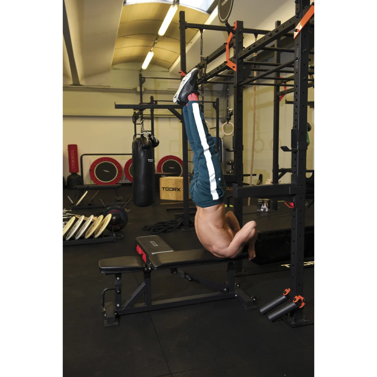 A man doing inverted rows on a bench in a gym, with gym equipment in the background.