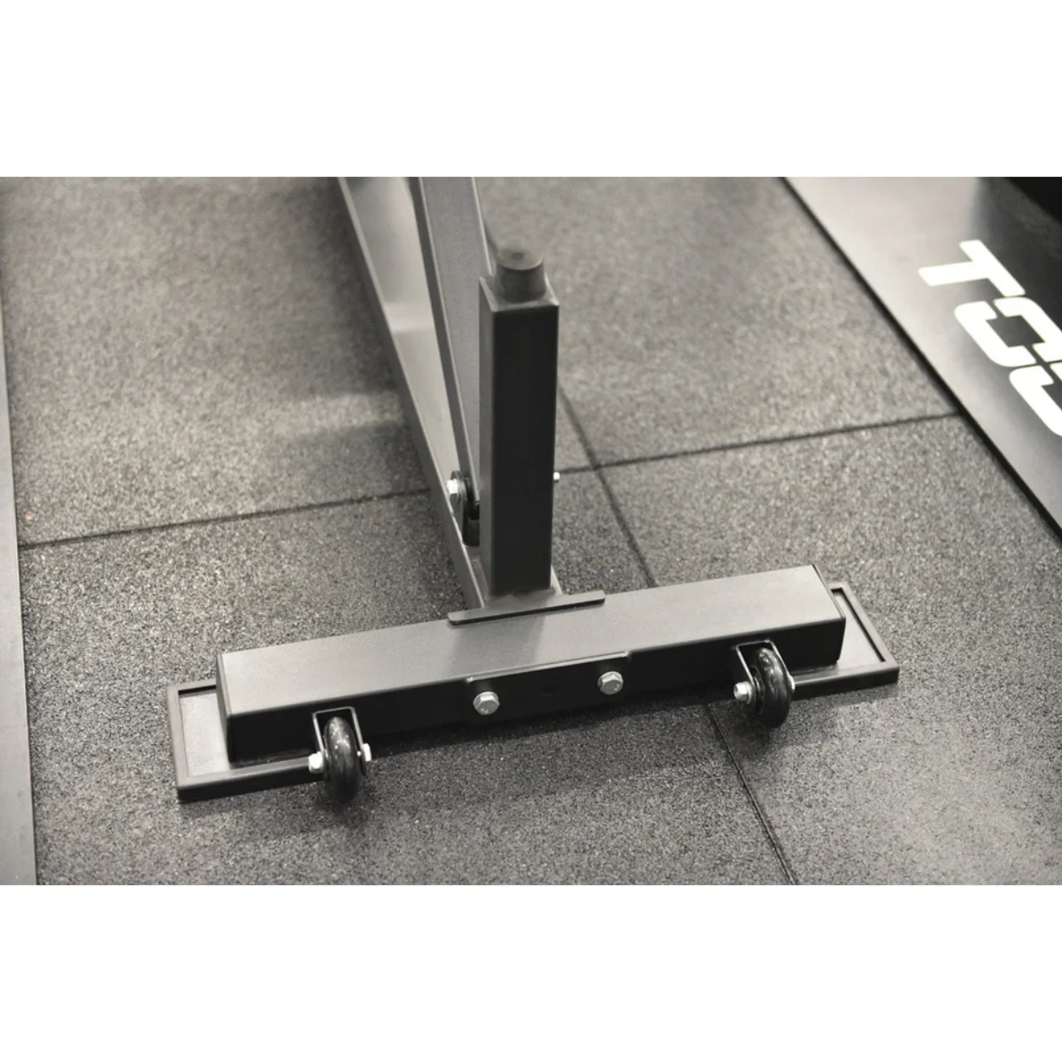 A black and gray gym equipment base with wheels on a gray floor.