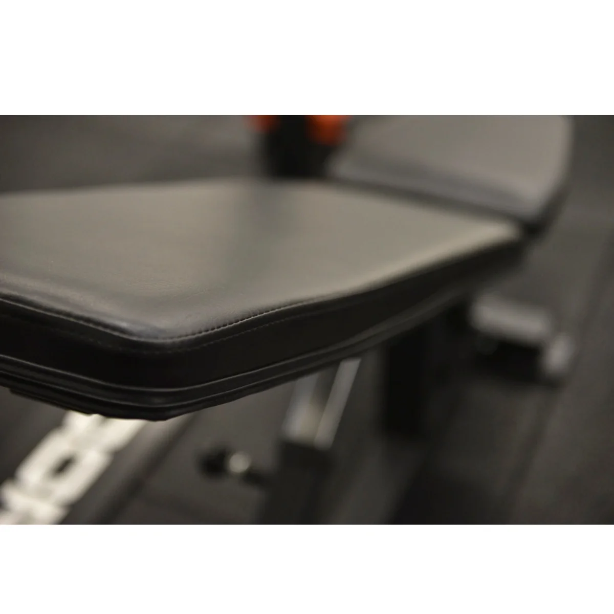 Close-up of a black weight bench seat with stitching, blurry background.