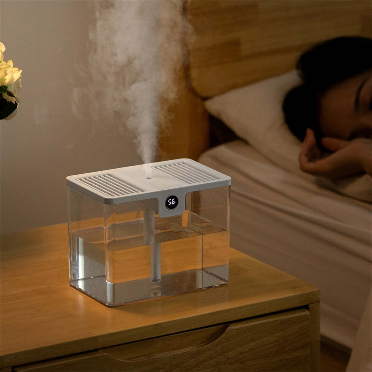 Luftbefeuchter auf einem Nachttisch mit Nebel, neben einer schlafenden Person im Bett.
