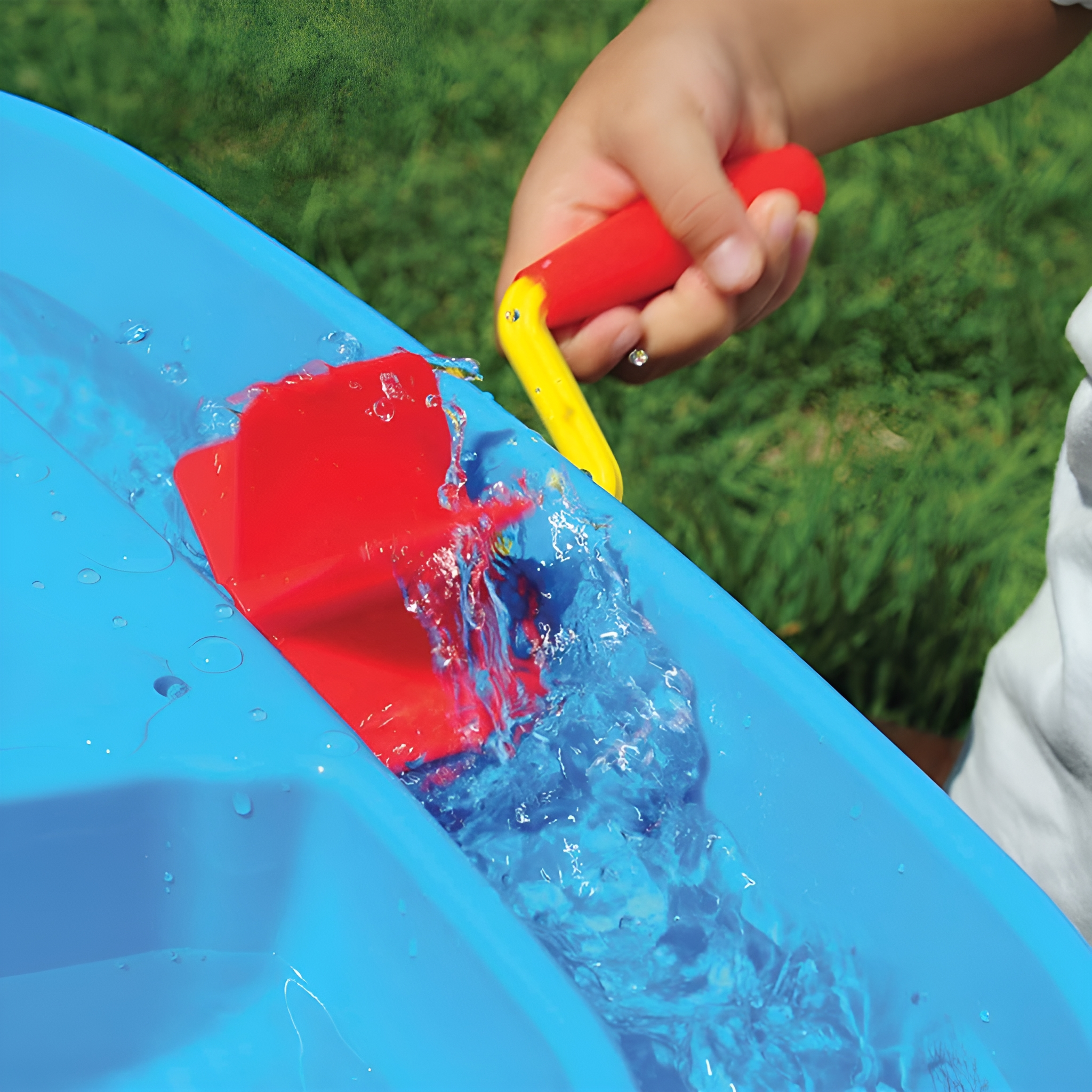 Ein Kinderhand, die ein rot-gelbes Spielzeug benutzt, um Wasser in einen blauen Wasserspieltisch zu gießen.