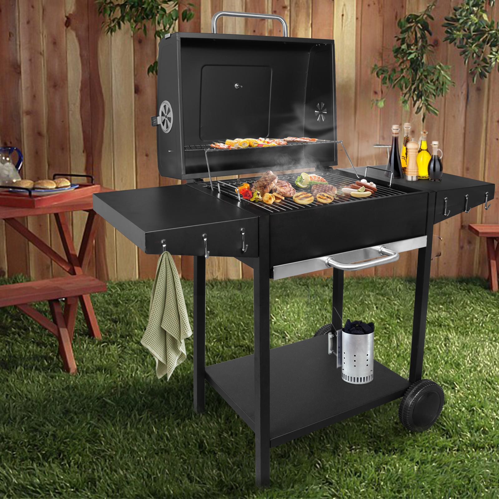 Schwarzer Holzkohlegrill mit Essen, auf einer Wiese vor einem Holzzaun.