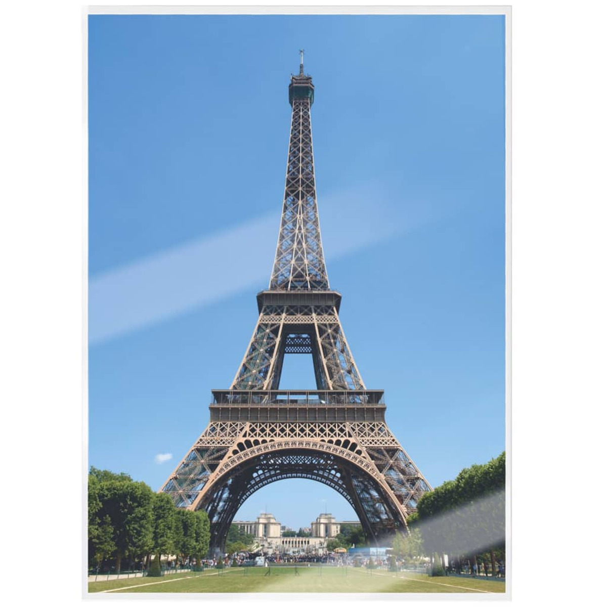 Der Eiffelturm in Paris vor blauem Himmel. Grüne Bäume im Vordergrund.