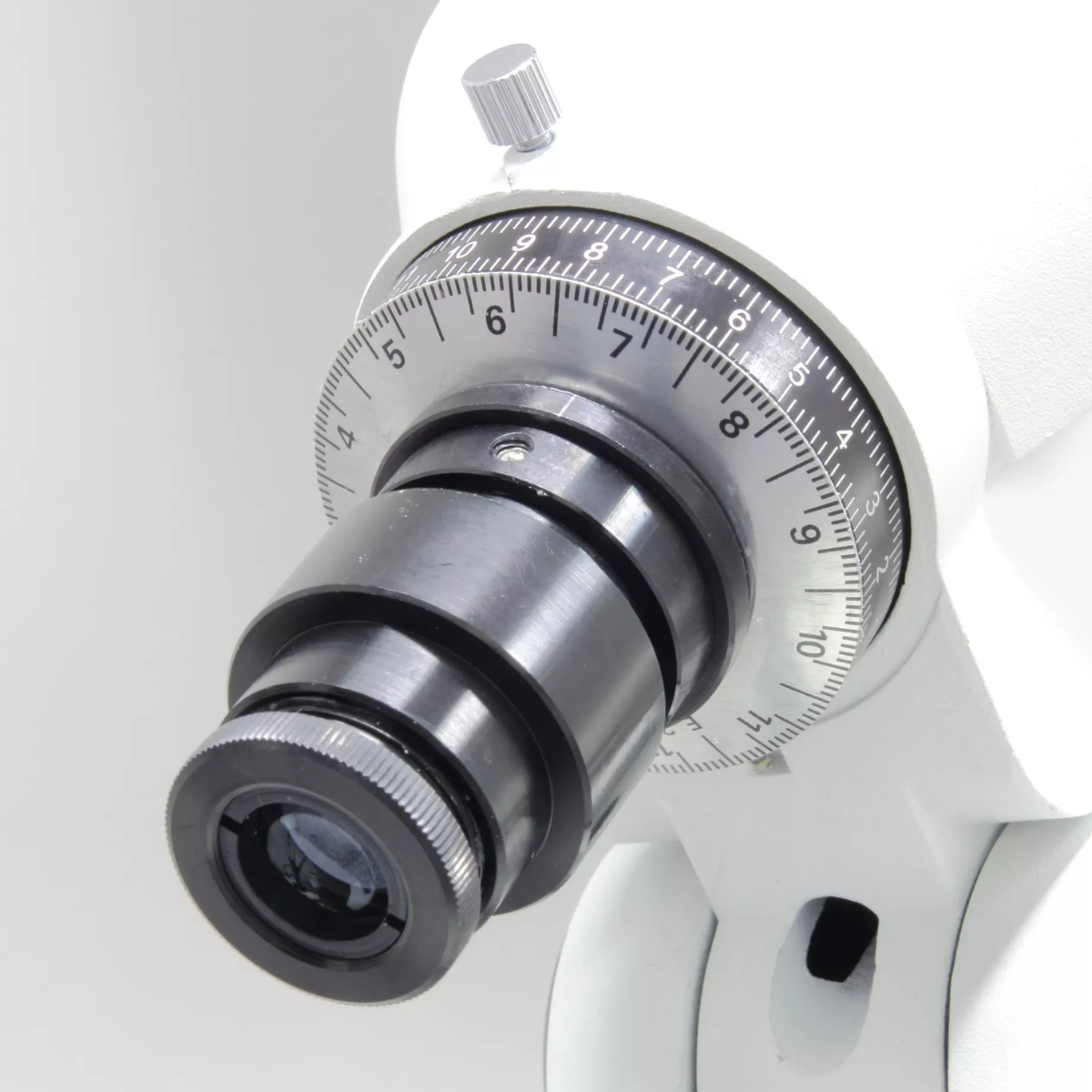 Vista de cerca del ocular ajustable de un telescopio con diales numerados. Fondo blanco.
