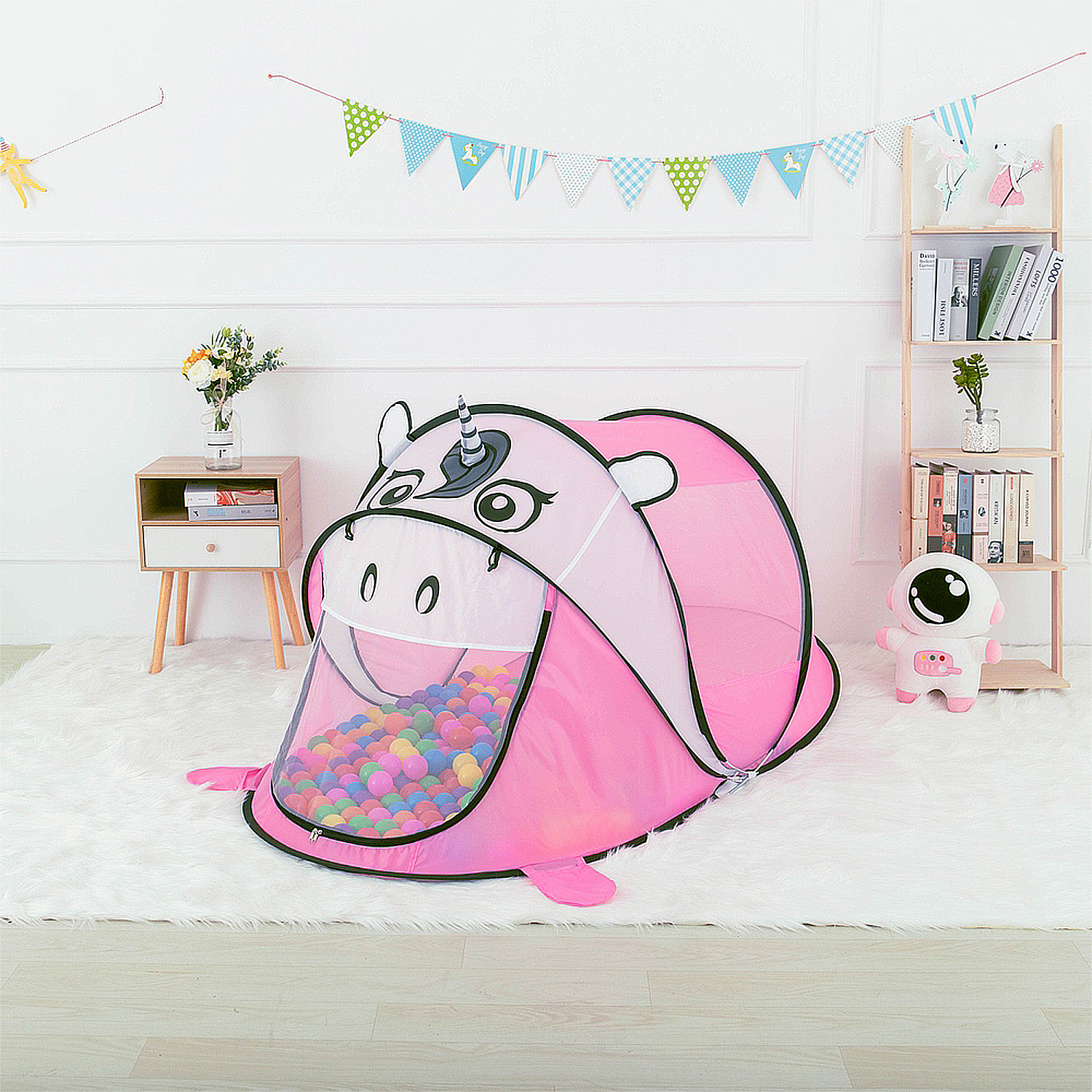 Tienda de campaña de unicornio rosa con bolas de colores dentro, sobre una alfombra blanca.
