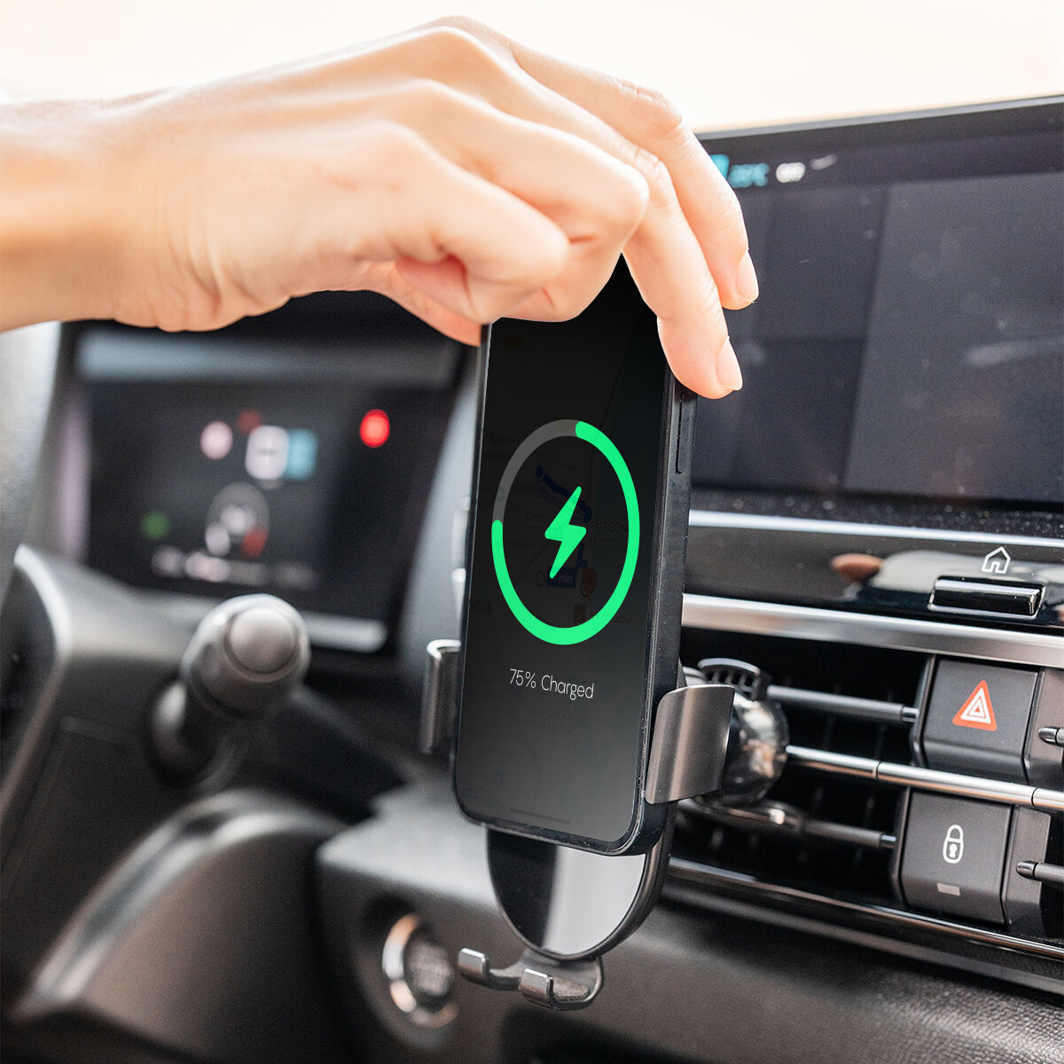 Una mano che tiene un telefono in carica wireless in un'auto. Il telefono mostra un indicatore di carica.