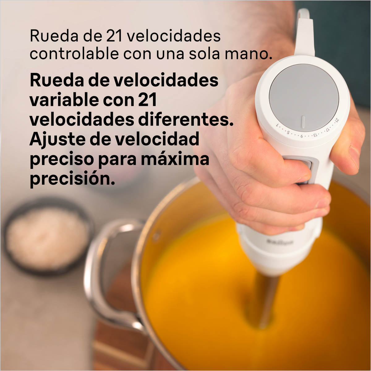 Ręka trzyma biały blender zanurzeniowy, mieszając żółty płyn w garnku.