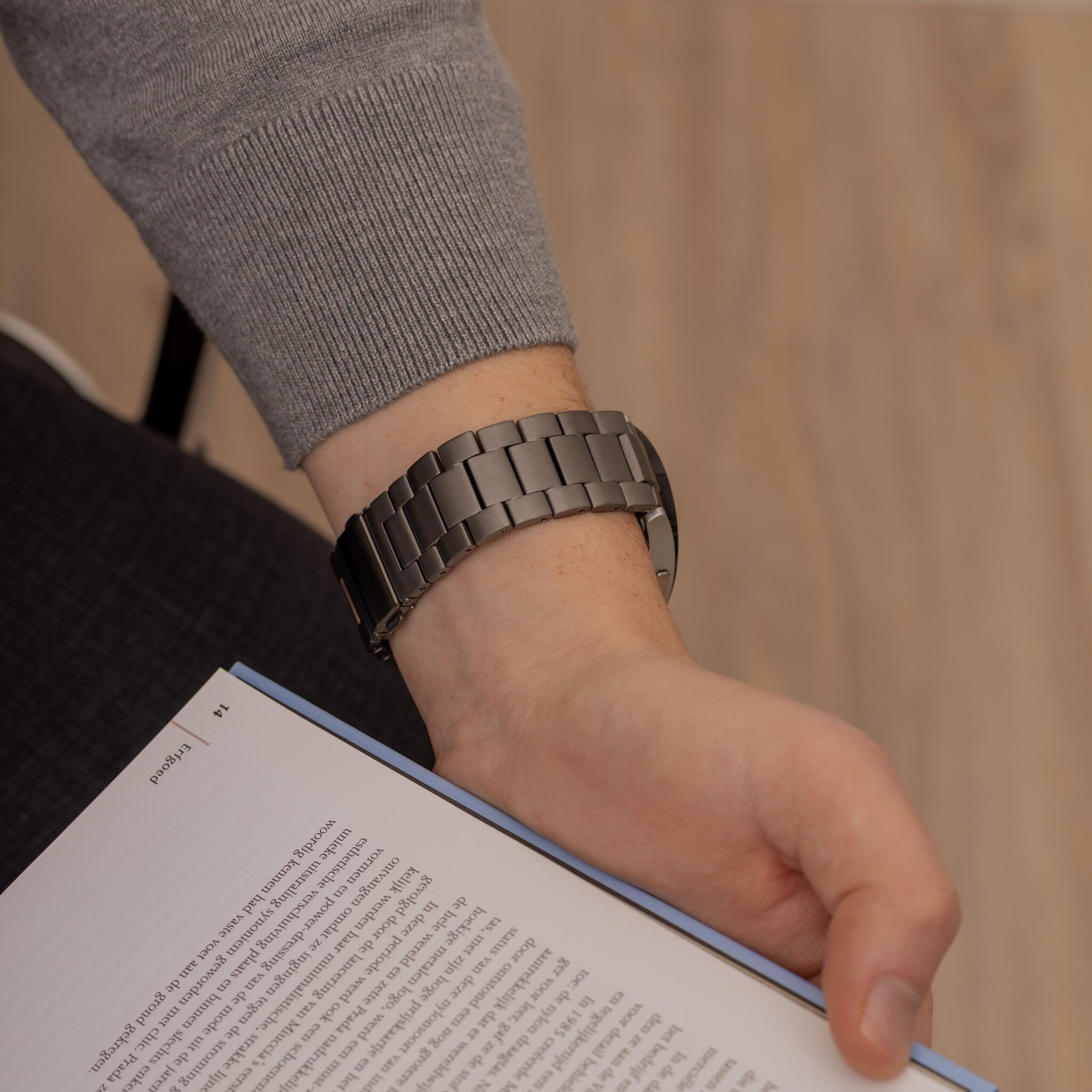 Ein Mann trägt eine Uhr und hält ein Buch. Das Armband der Uhr ist aus Metall.