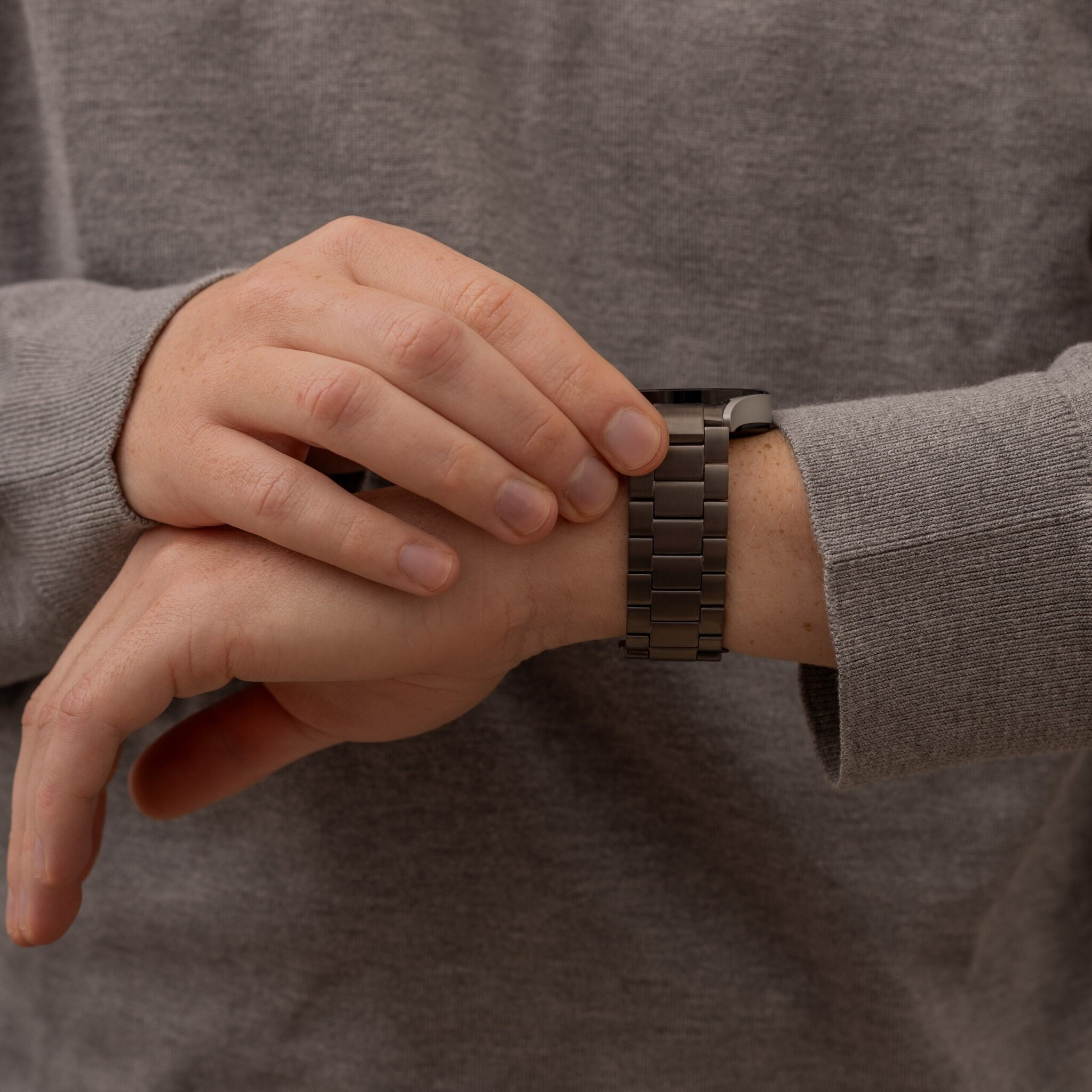 Eine Person in einem grauen Pullover trägt eine Uhr am Handgelenk. Die Uhr ist dunkelgrau.
