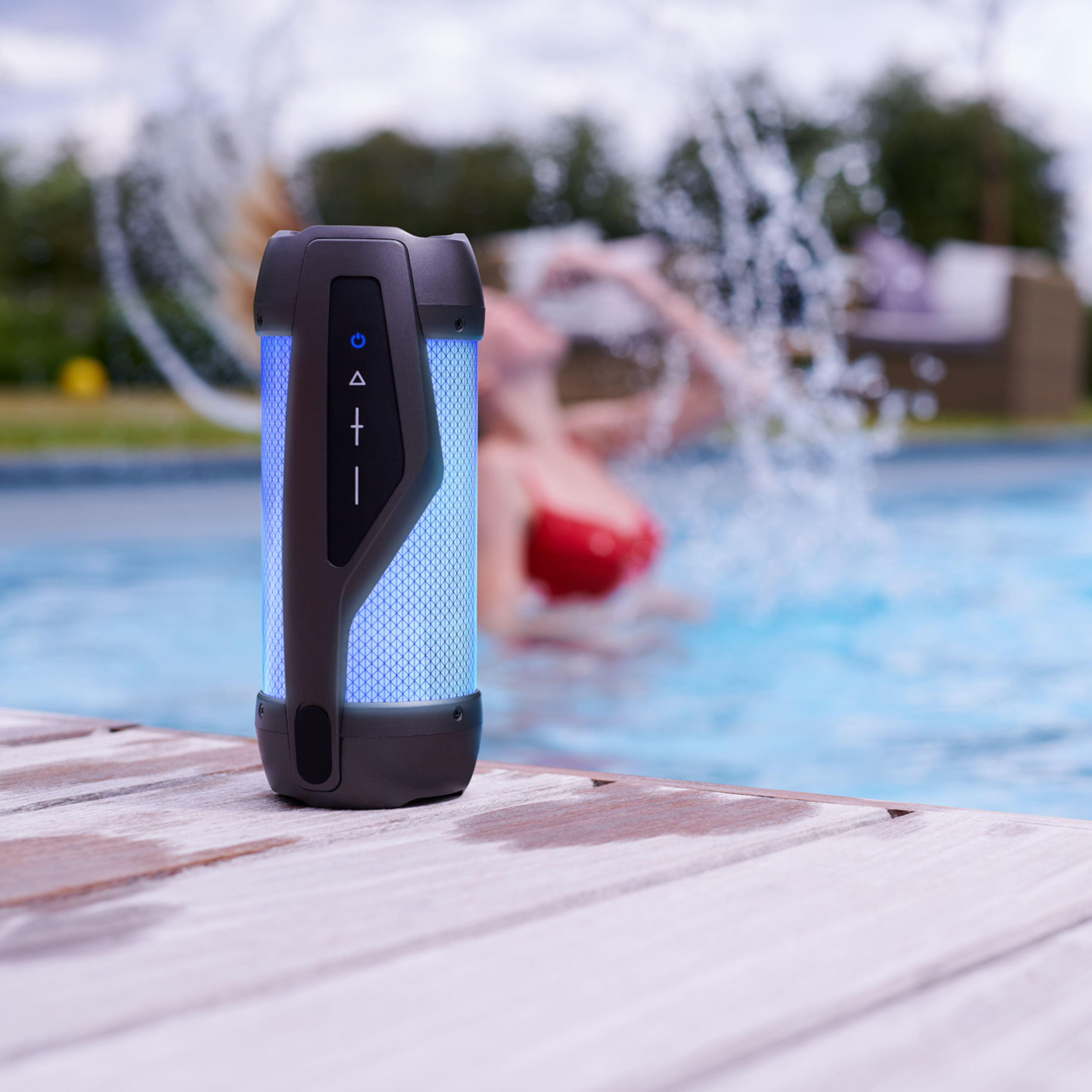 Buitenspeaker naast zwembad. Persoon in rode bikini zwemt op de achtergrond.