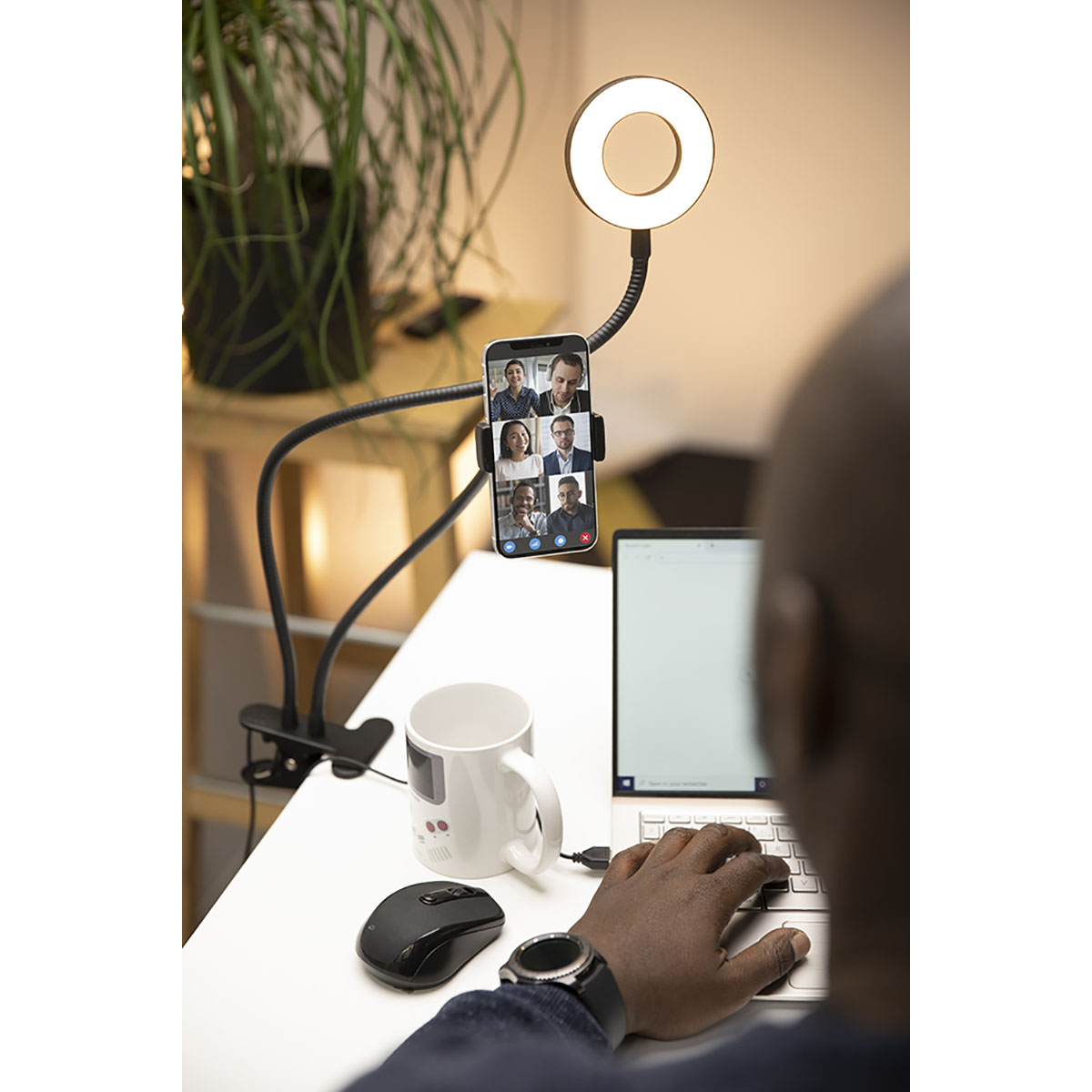 Eine Person, die ein Laptop- und Ringlicht-Setup mit einem Smartphone auf einem Schreibtisch verwendet. Videoanruf auf dem Bildschirm.