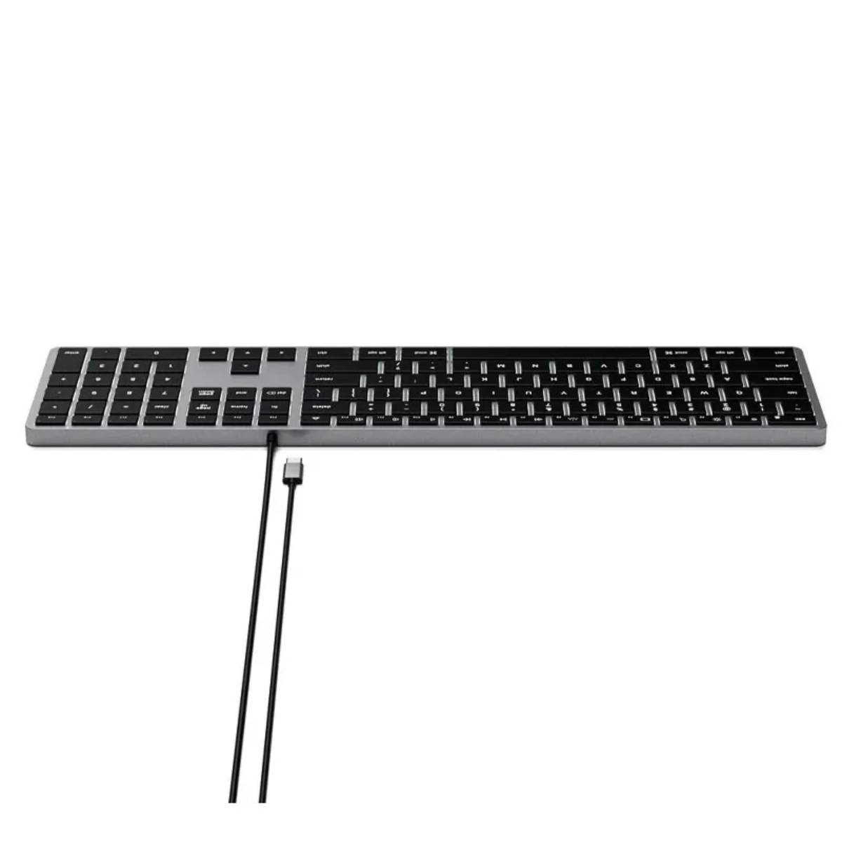 Un teclado plateado y negro. El teclado tiene un cable USB-C conectado y un fondo blanco.