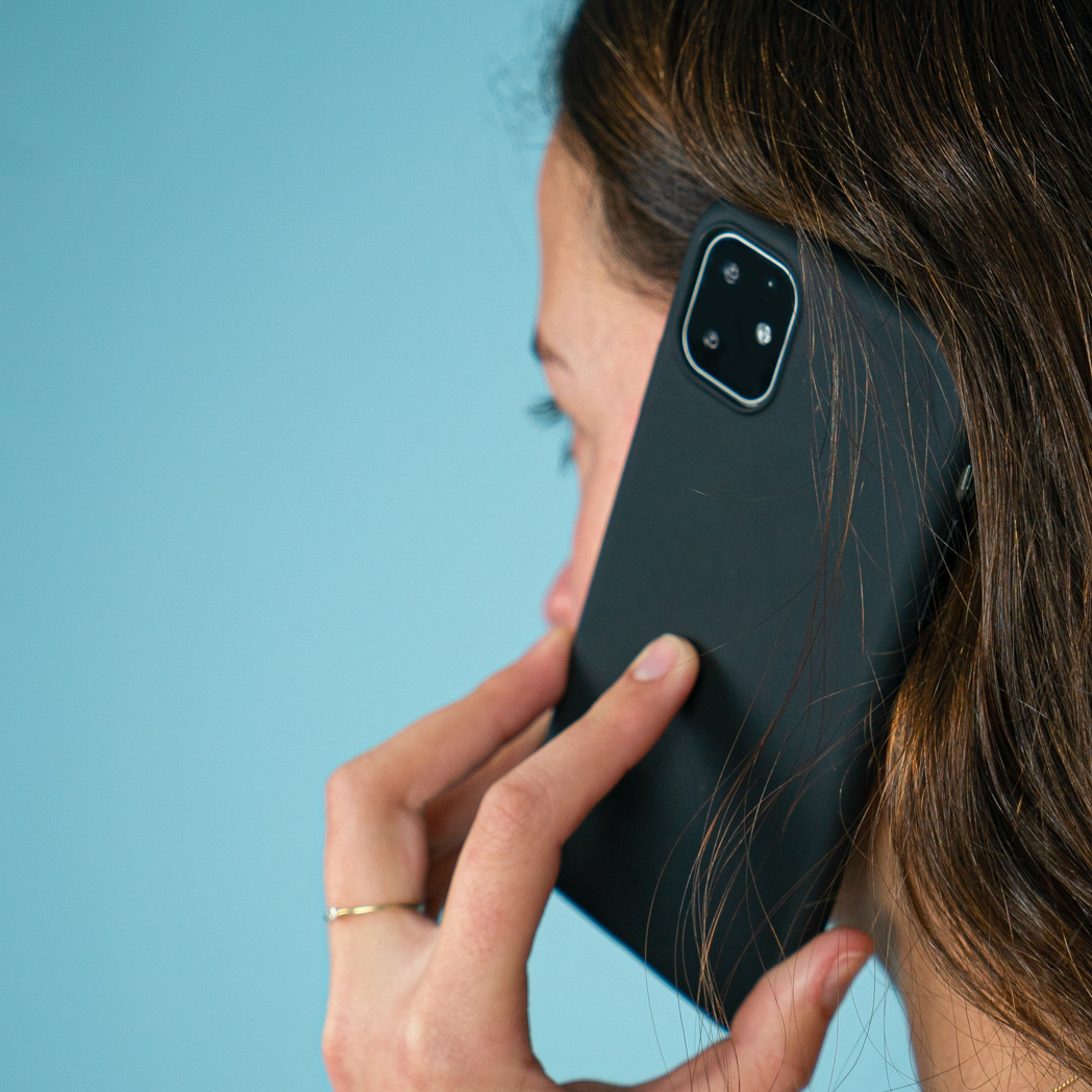 Vrouw die een zwarte telefoon aan haar oor houdt, zijaanzicht.