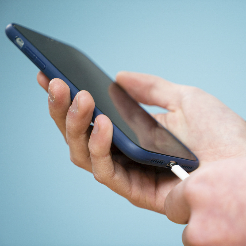 Een hand die een zwarte smartphone vasthoudt met een witte oplaadkabel erin.