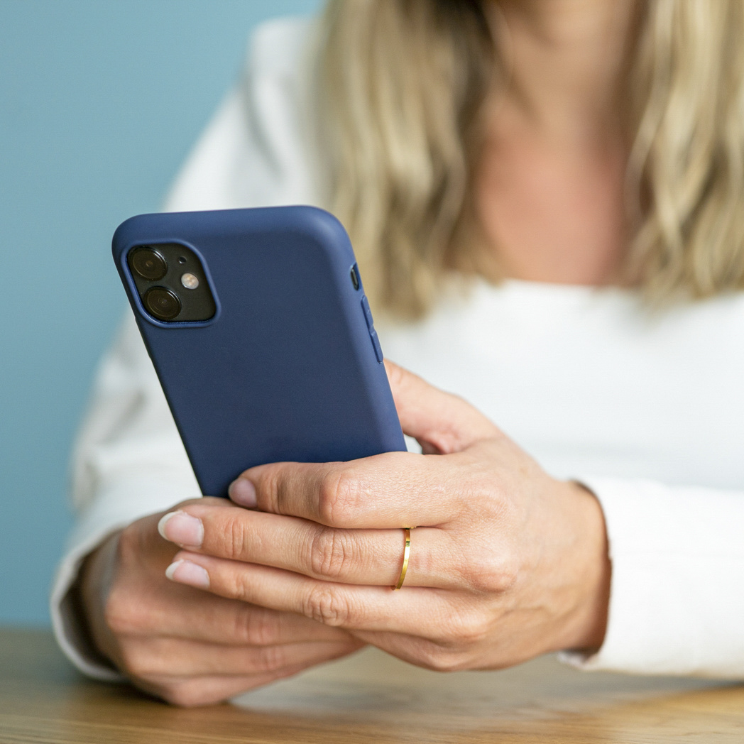 Een vrouw houdt een marineblauwe telefoon in haar handen. Ze draagt een wit overhemd en een gouden ring.